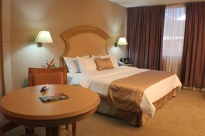 A hotel room with a bed, two bedside lamps, a round table with a magazine, and a chair.