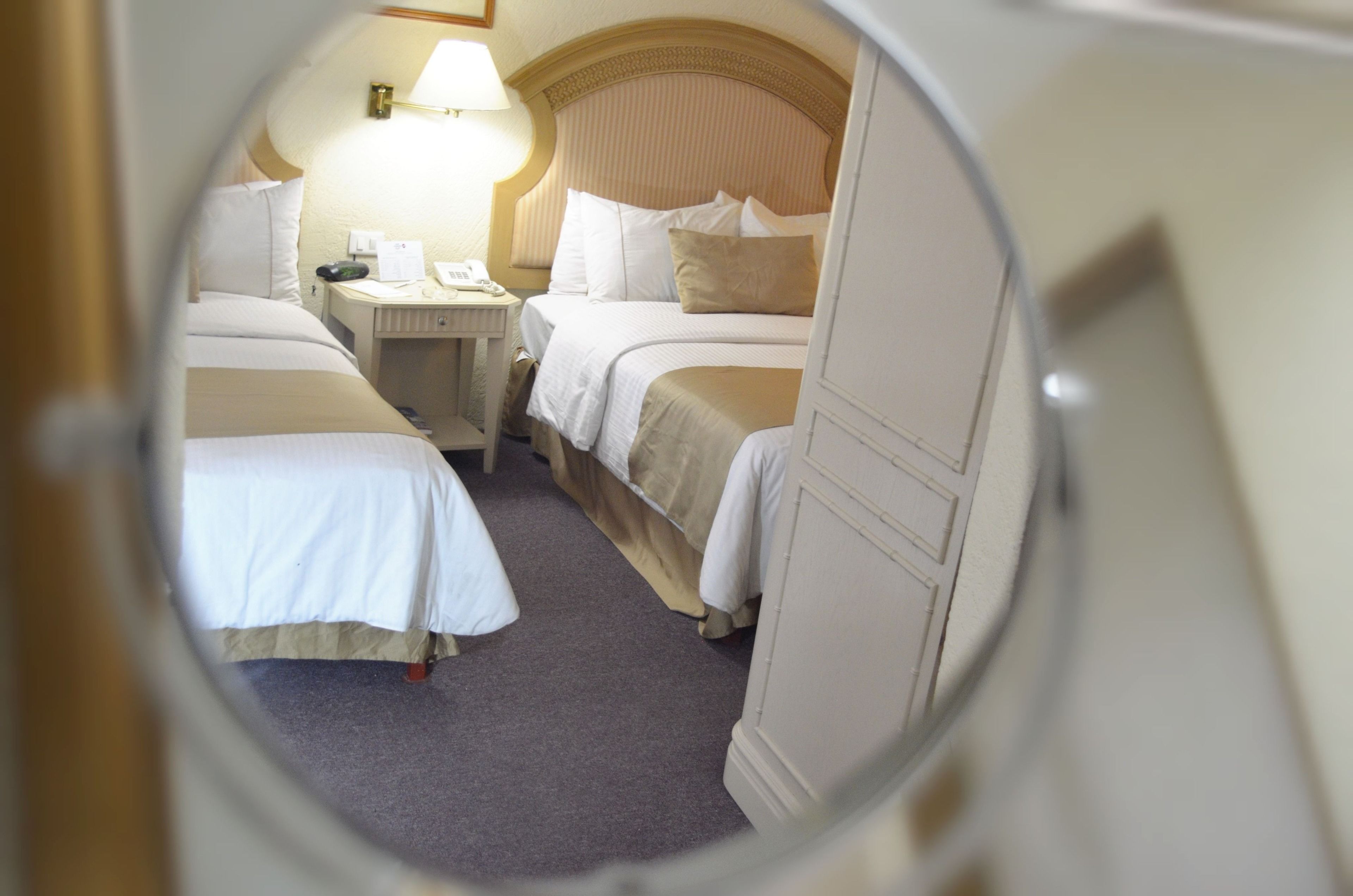 A circular view of a hotel room with two beds, a nightstand, and a lamp.