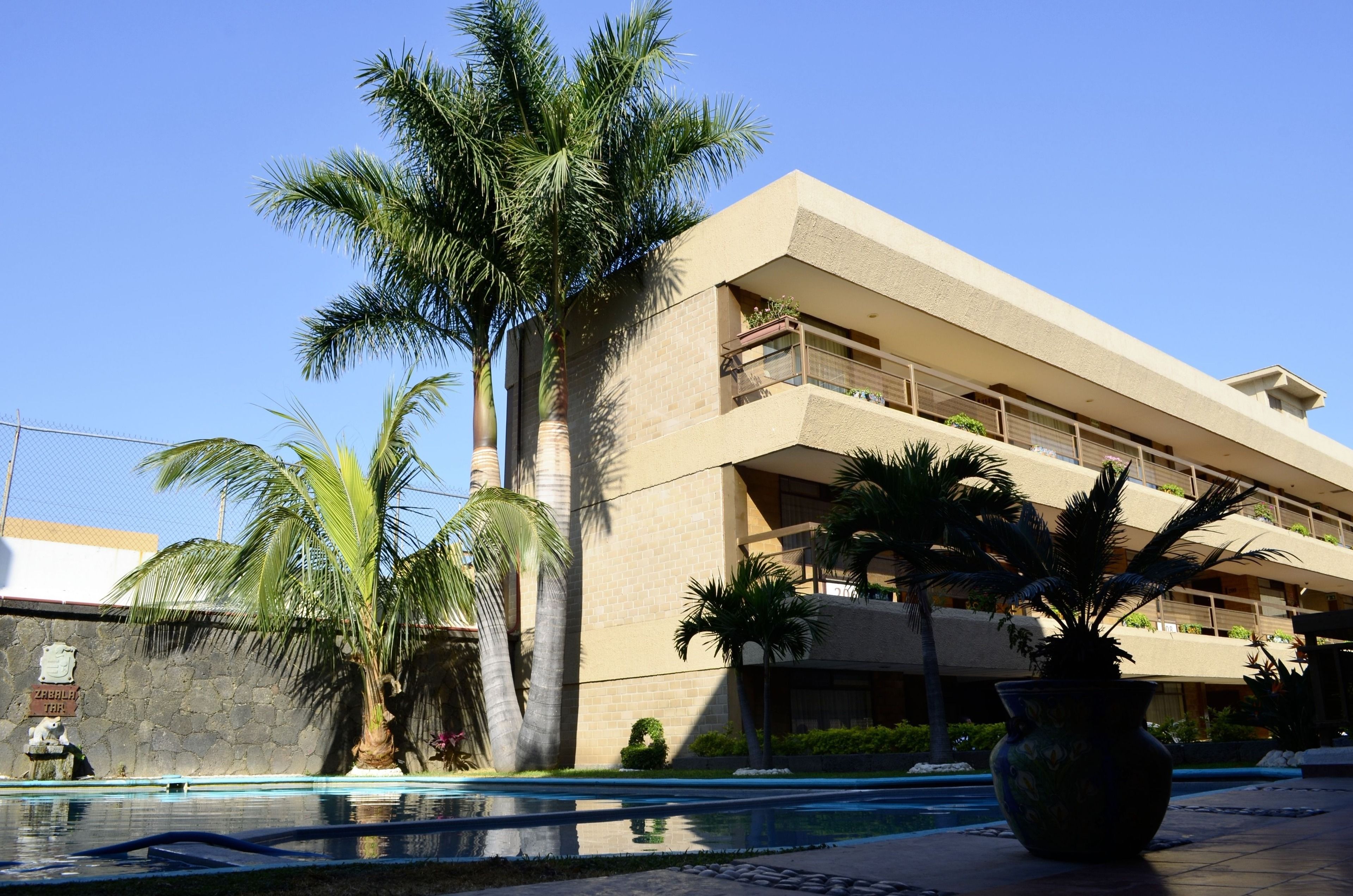 Un hotel con piscina, palmeras y un muro de piedra.