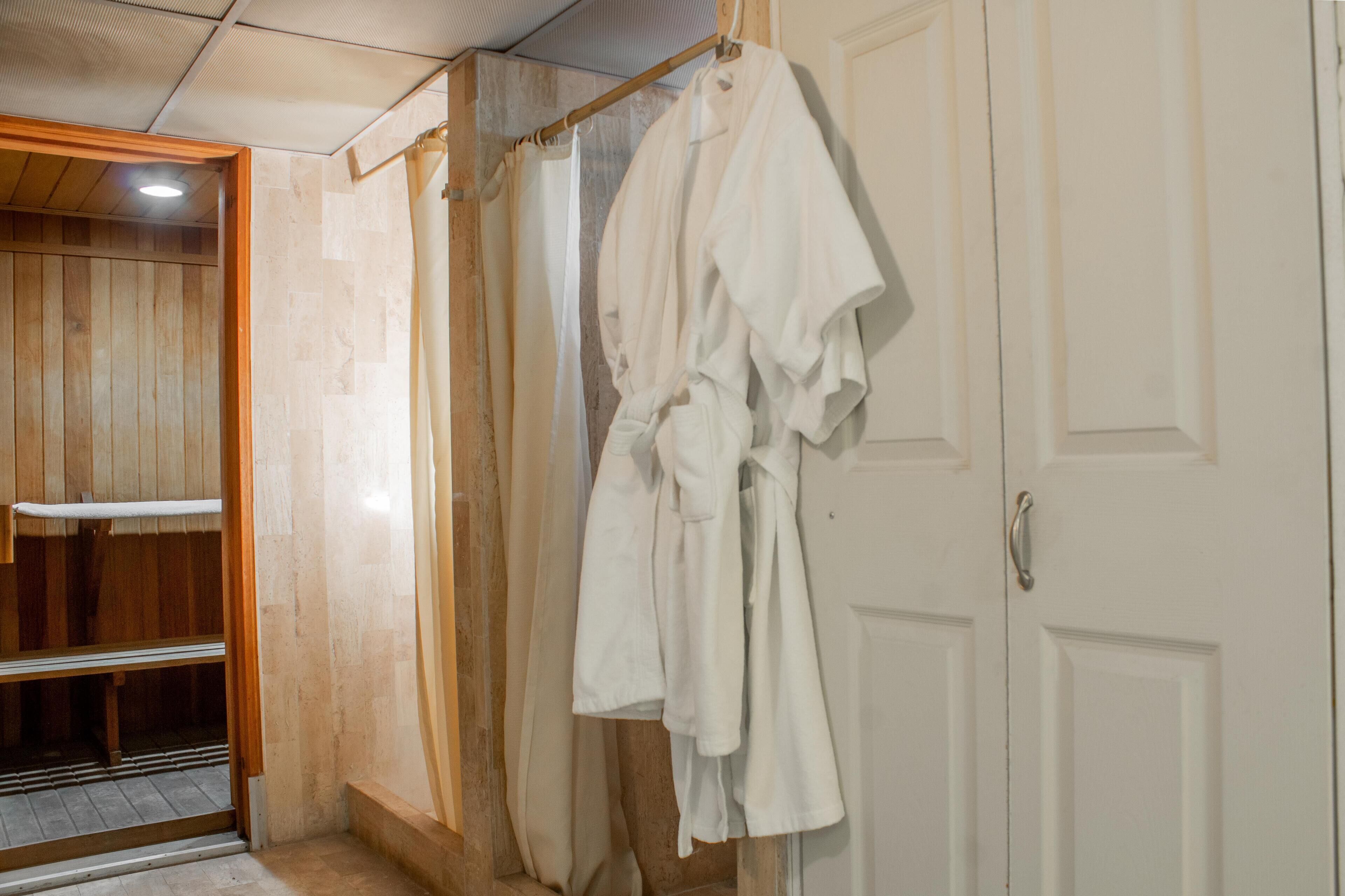 Un baño con cabina de ducha de madera, una bañera blanca y una bata blanca colgada en una puerta.