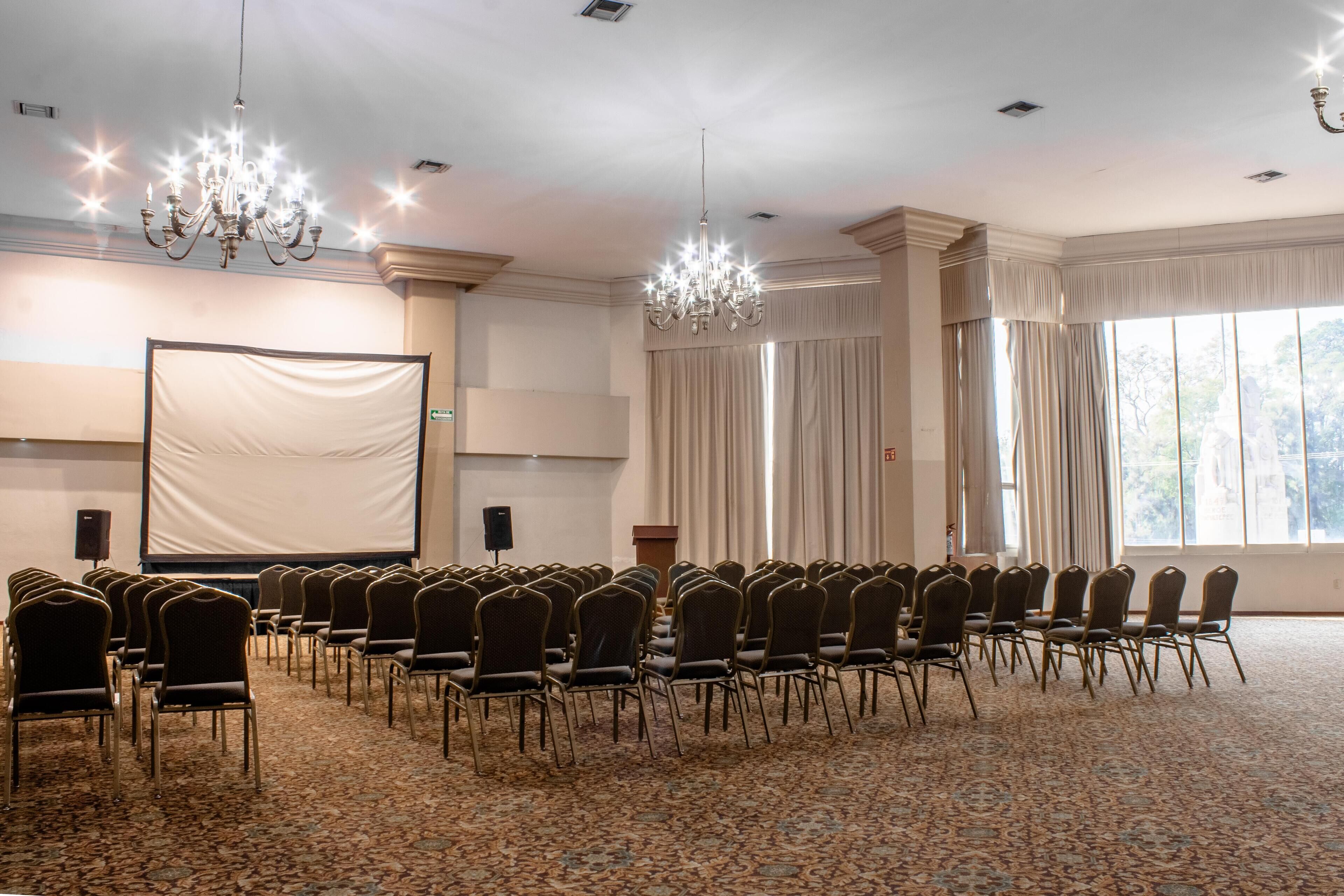 A conference room with rows of chairs, a large screen, and two chandeliers.