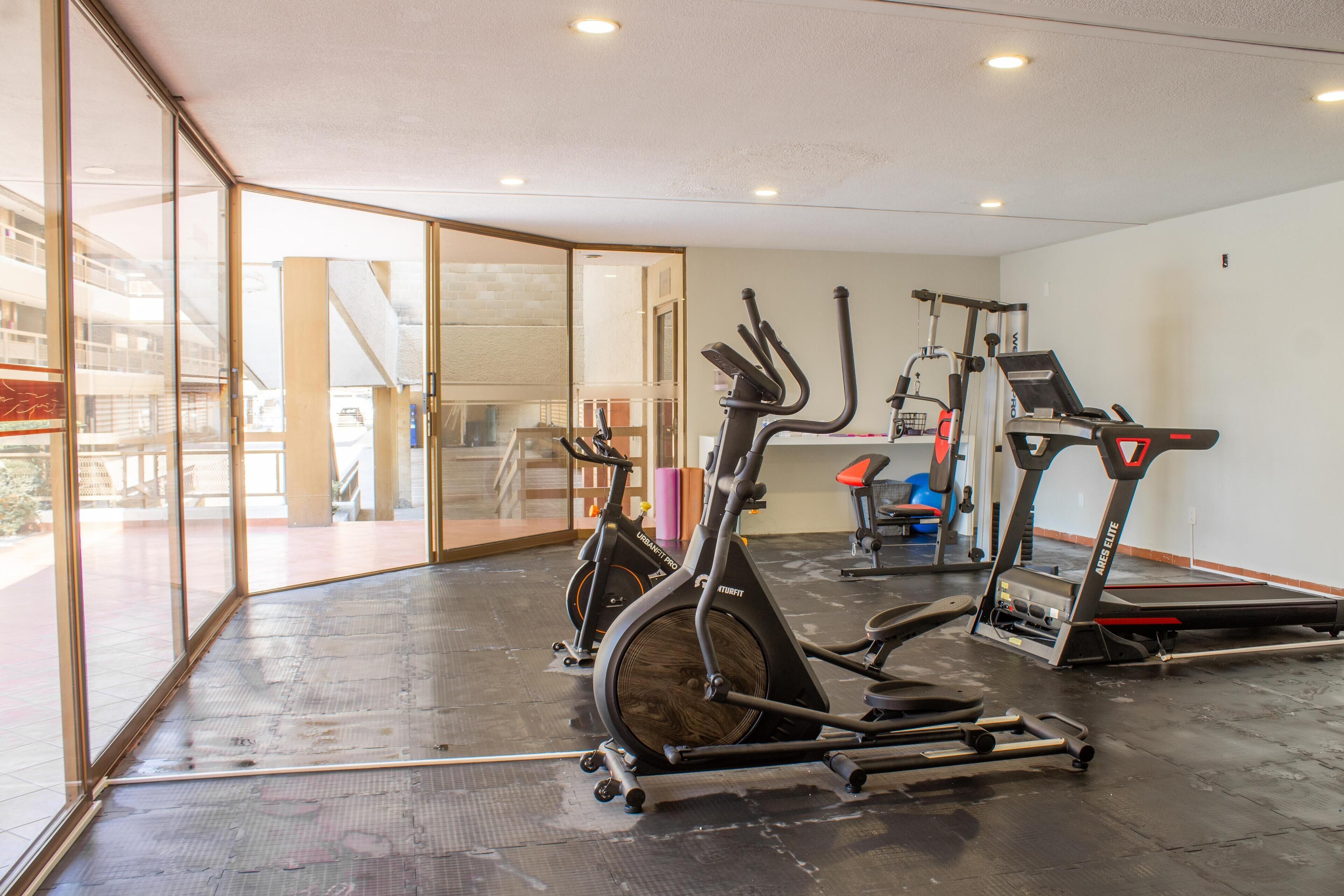 Un gimnasio con equipamiento de ejercicio, paredes de vidrio y vistas al exterior.