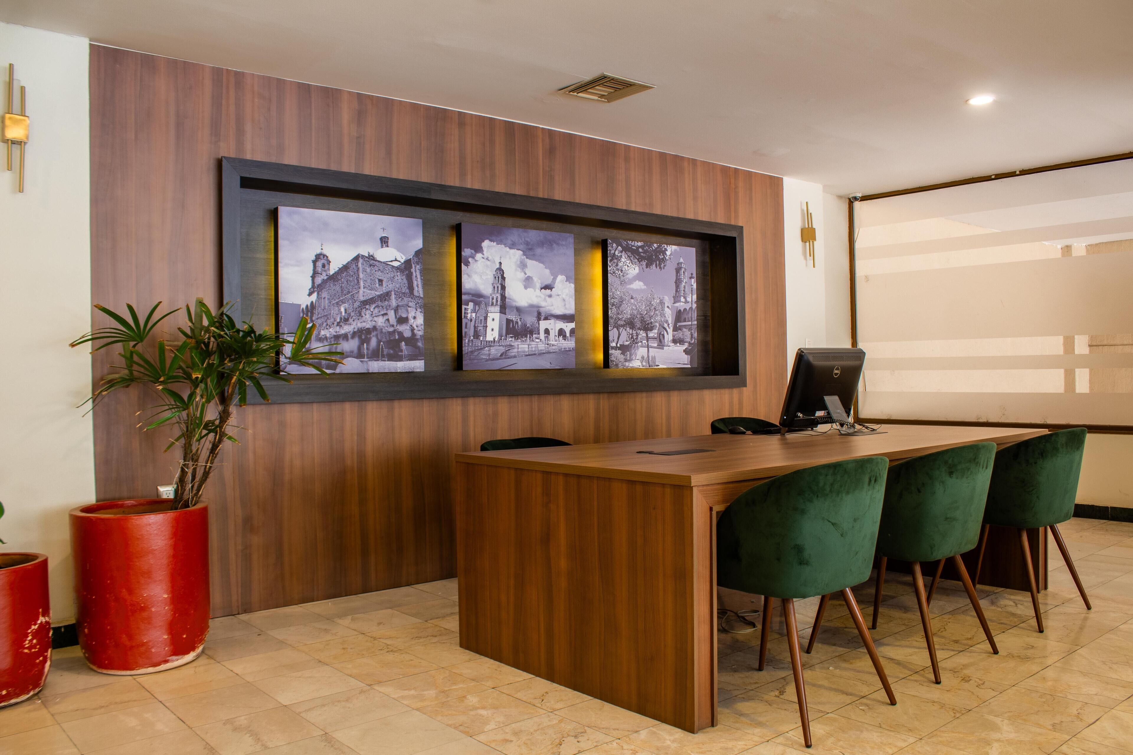 A reception area with a wooden reception desk, three framed black and white photographs on the wall, and a potted plant.