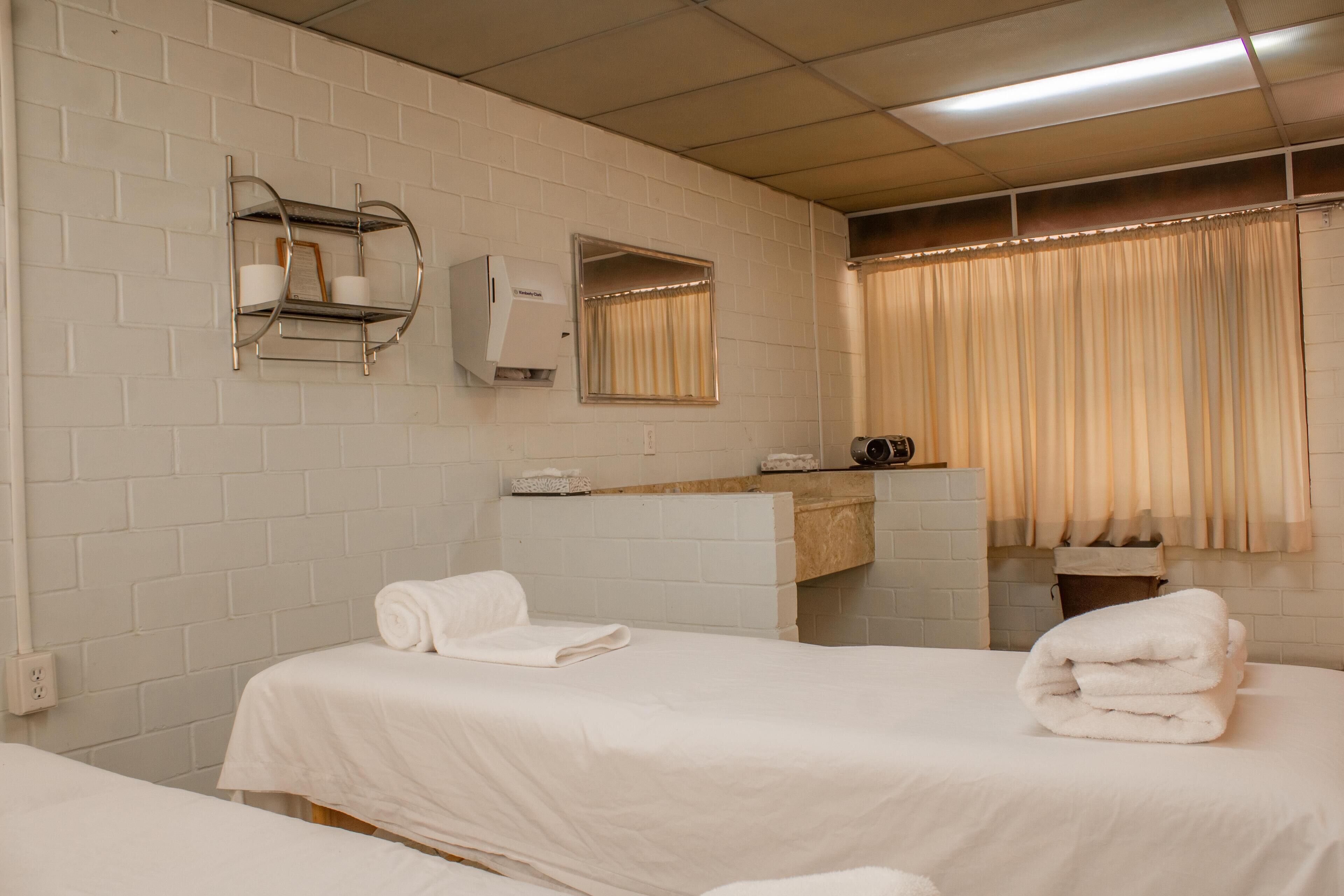 Une chambre d’hôtel avec deux lits, une salle de bain avec un miroir, un porte-serviettes et une fenêtre avec des rideaux.