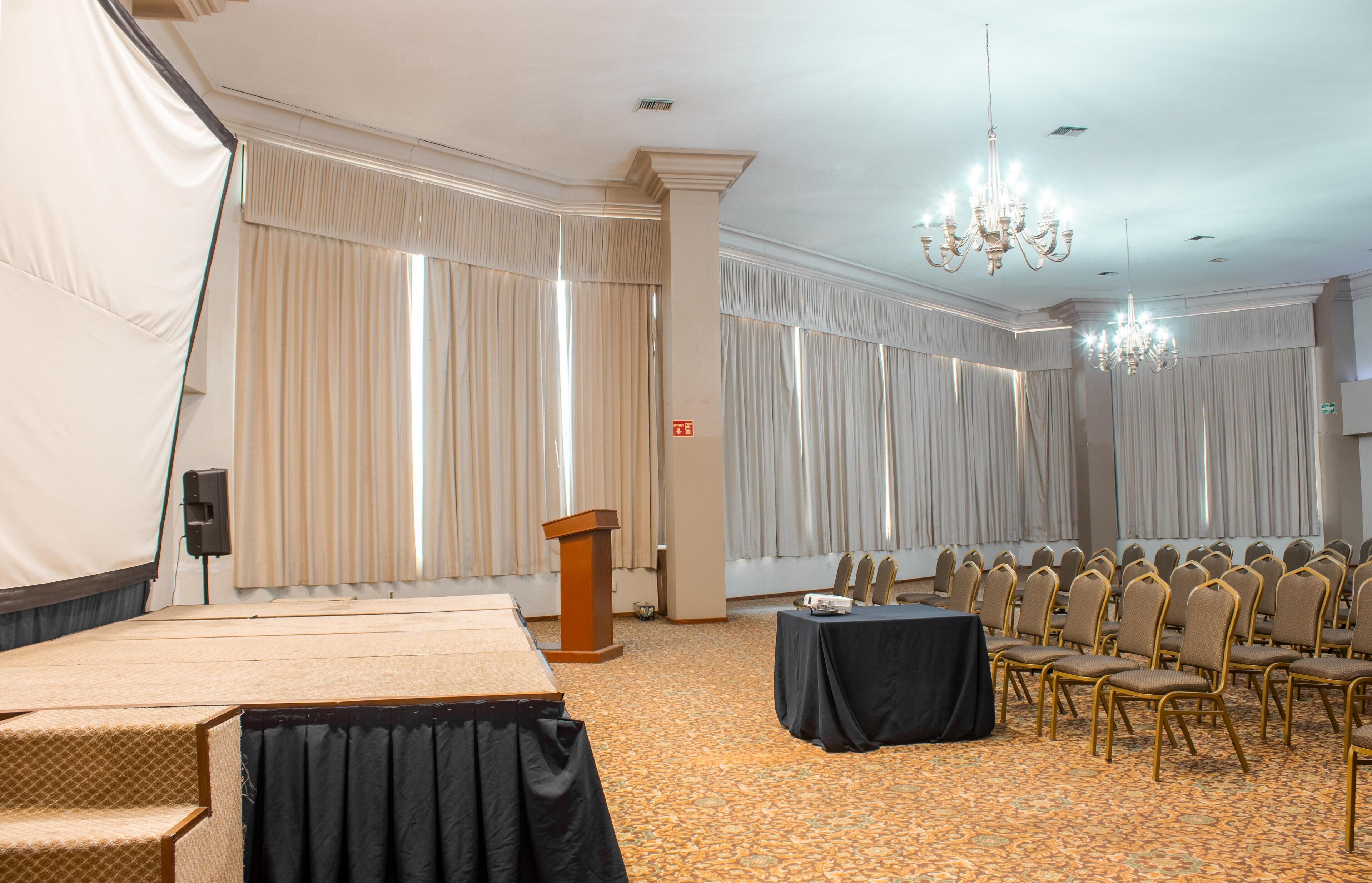 A conference room with a stage, a podium, rows of chairs, and a carpeted floor.