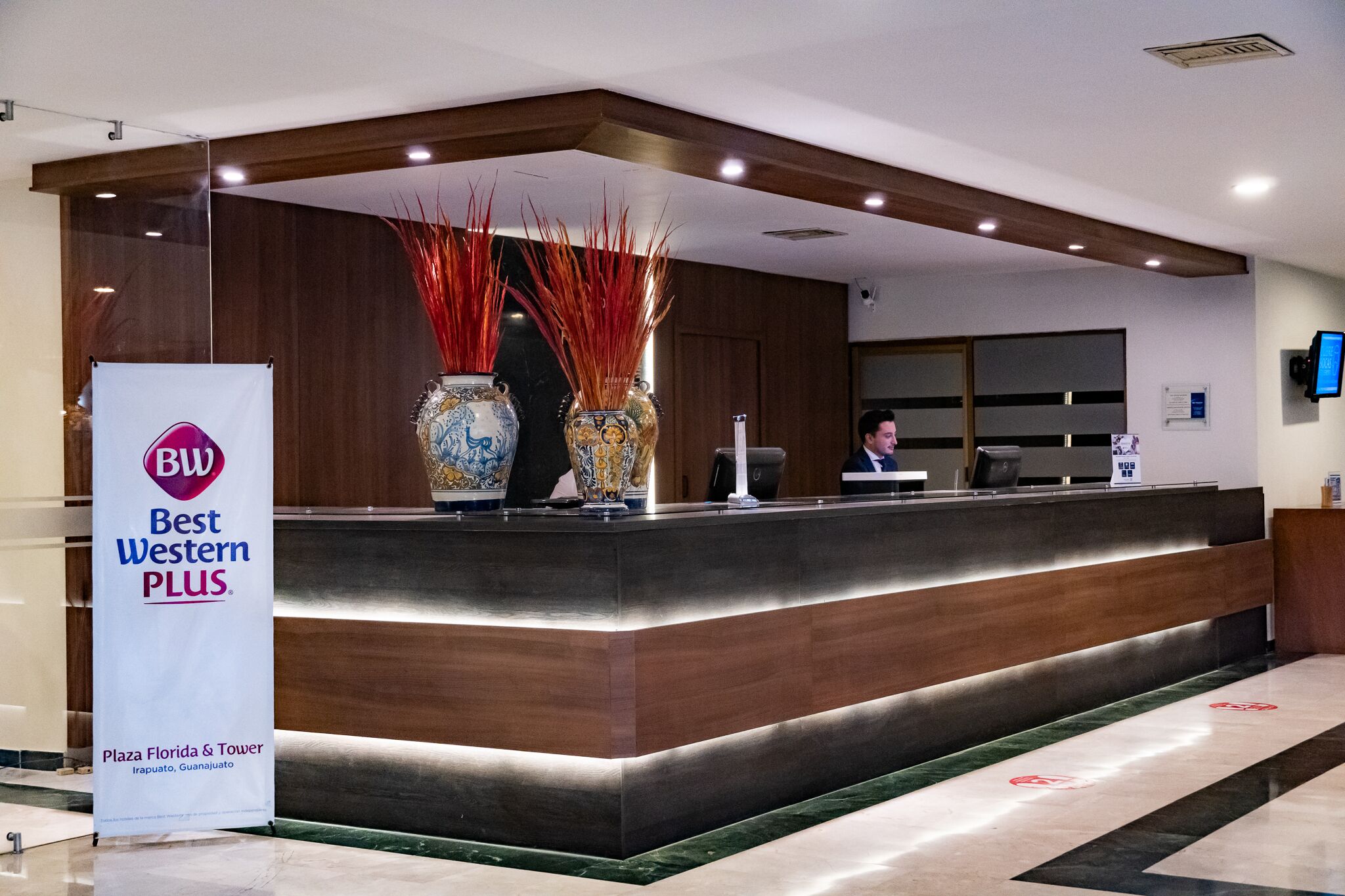 Una recepción con el letrero de Best Western PLUS, un jarrón con detalles decorativos y un monitor en la pared.