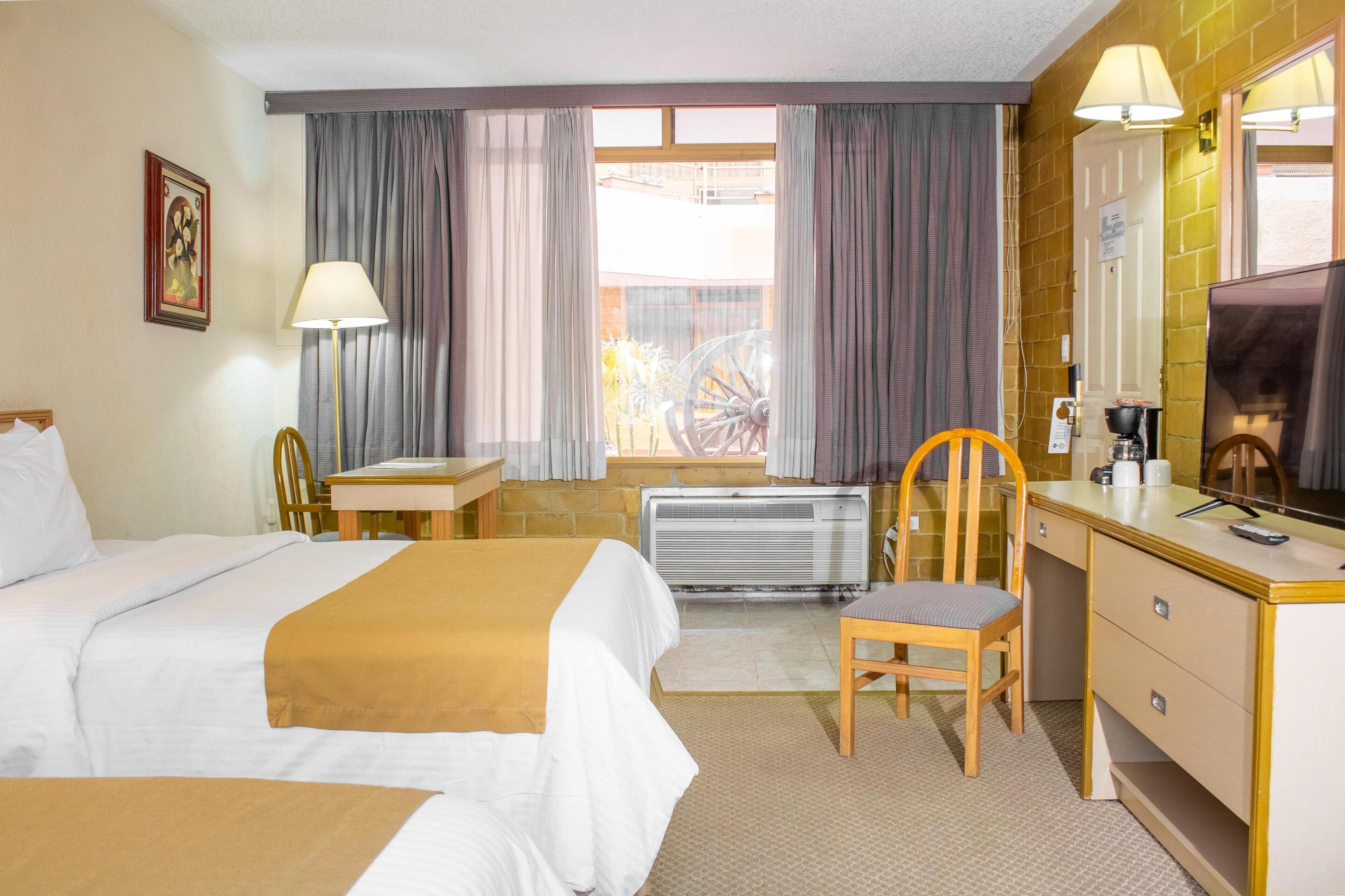 A hotel room with two beds, a desk, a chair, a TV, and a window with curtains.