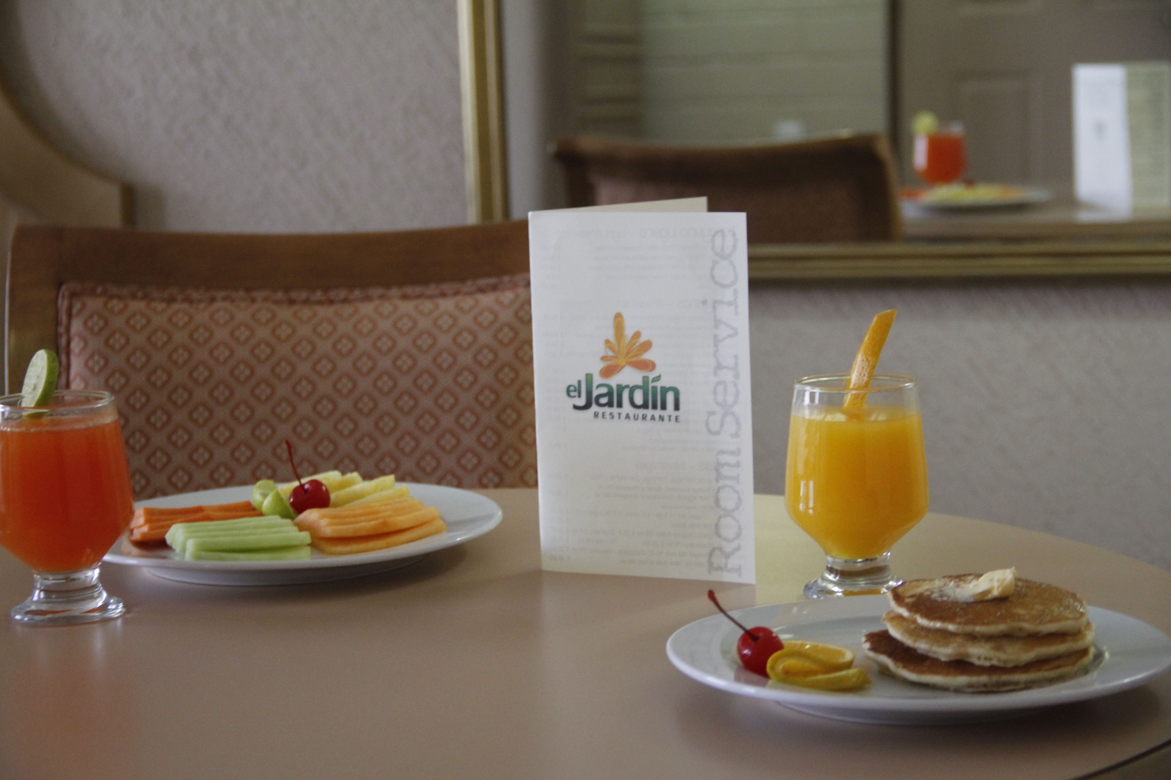 Un desayuno con un menú, un plato de fruta, panqueques y un vaso de jugo de naranja.