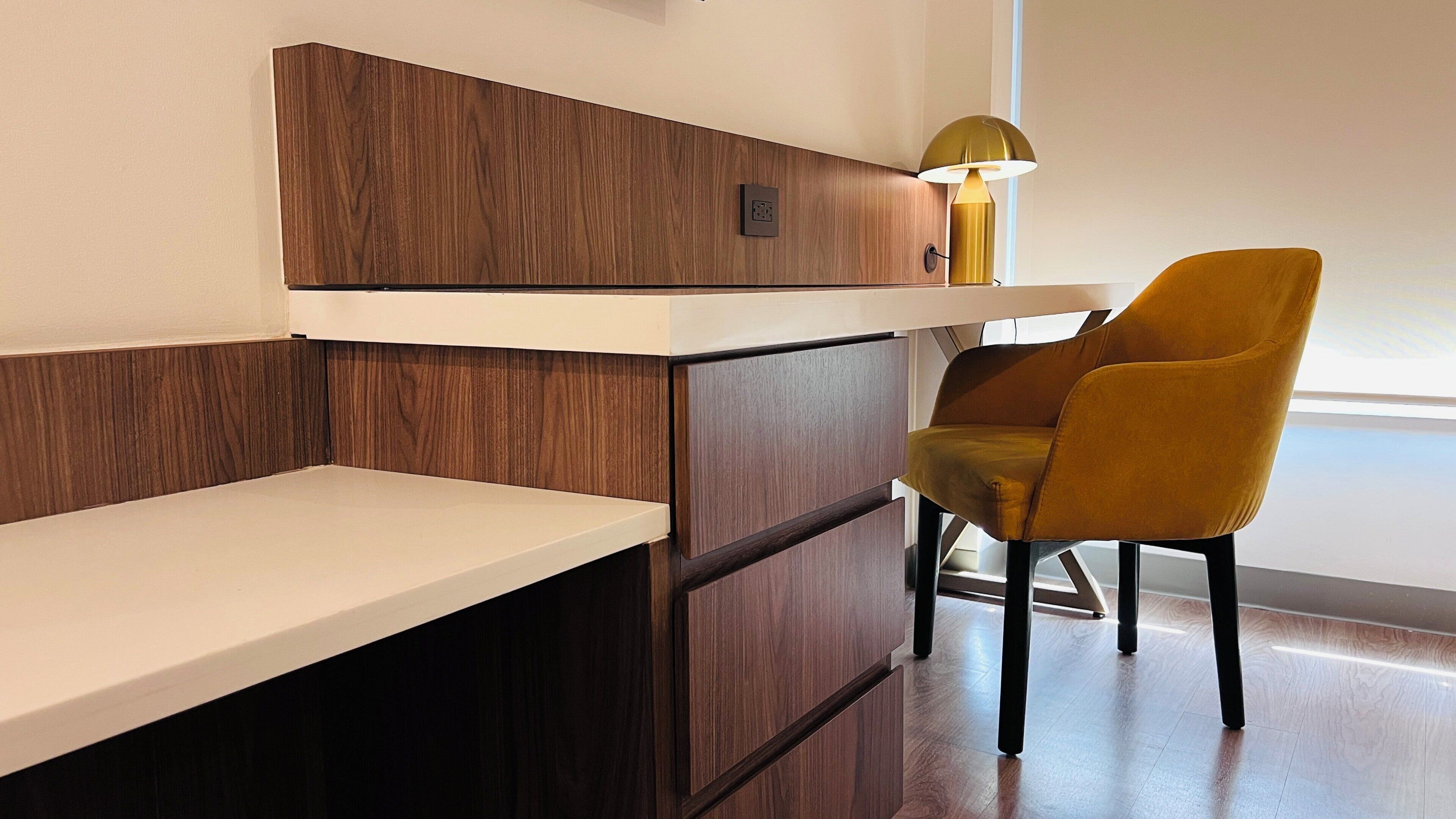 A modern room with a wooden accent wall, a white desk, a yellow chair, and a lamp.