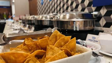 A bowl of tortilla chips with tongs, a white cup, and a blue and white tiled wall in the background.