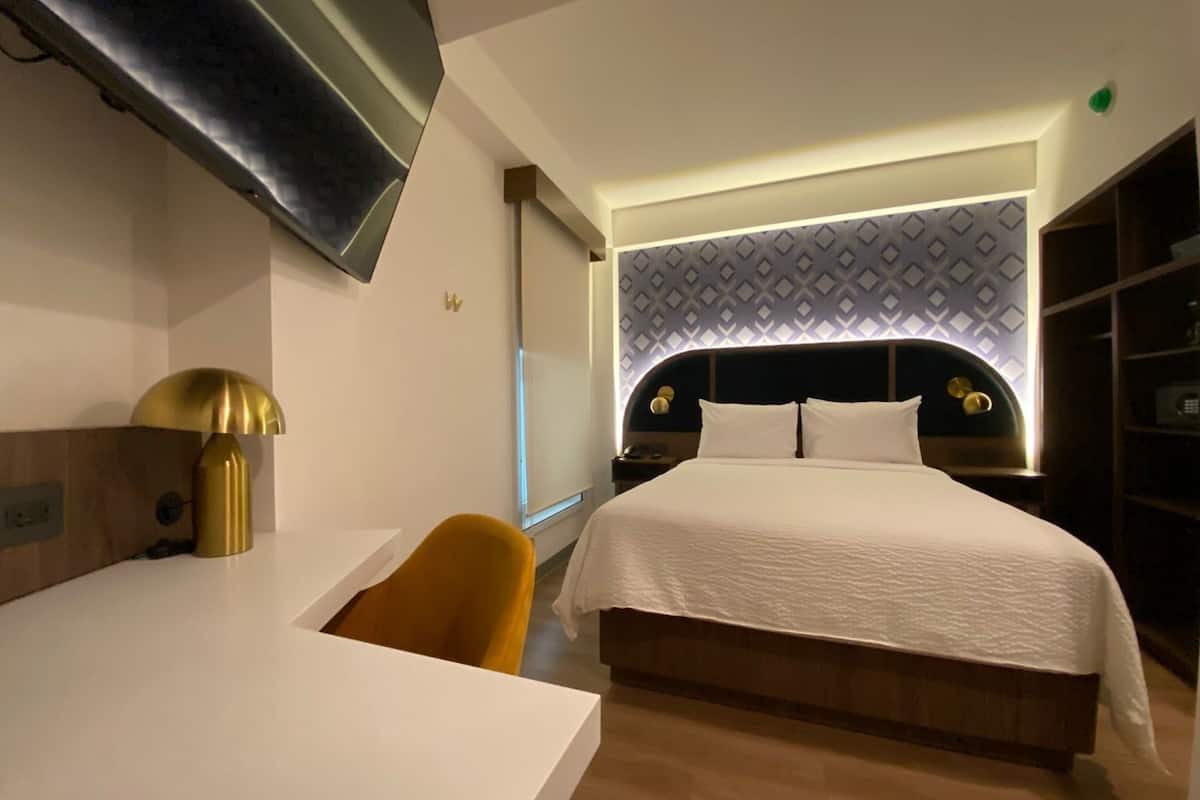 Una habitación de hotel moderna con una cama, un escritorio, una silla y un televisor montado en la pared.