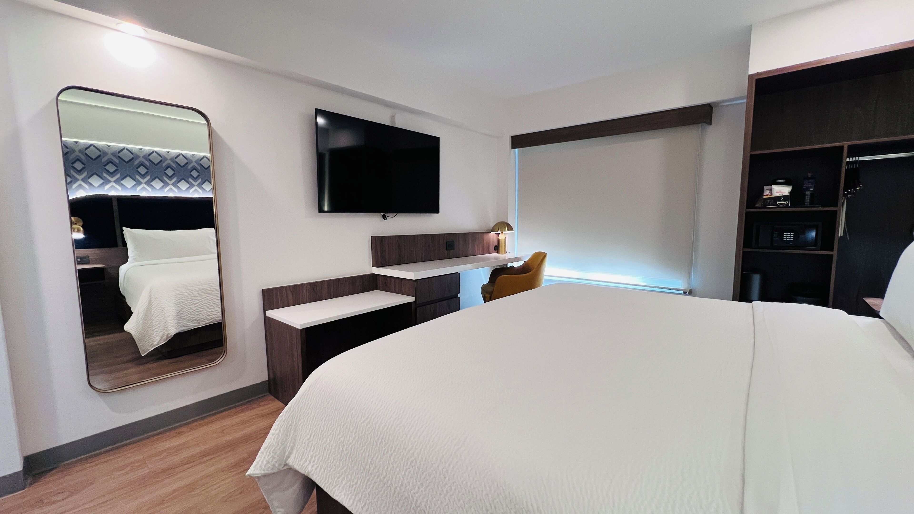 Une chambre d’hôtel équipée d’un lit, d’un bureau, d’une chaise, d’une télévision, d’une armoire et d’un miroir.