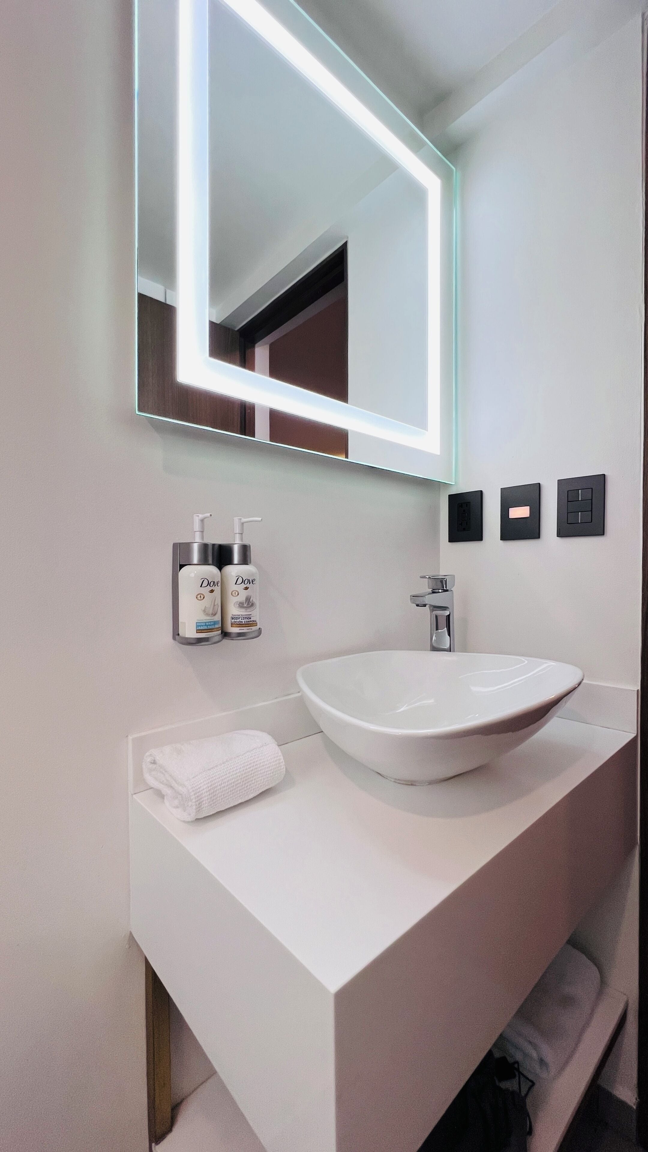 Un baño moderno con un espejo grande, un lavamanos blanco y dos dispensadores de loción Dove.
