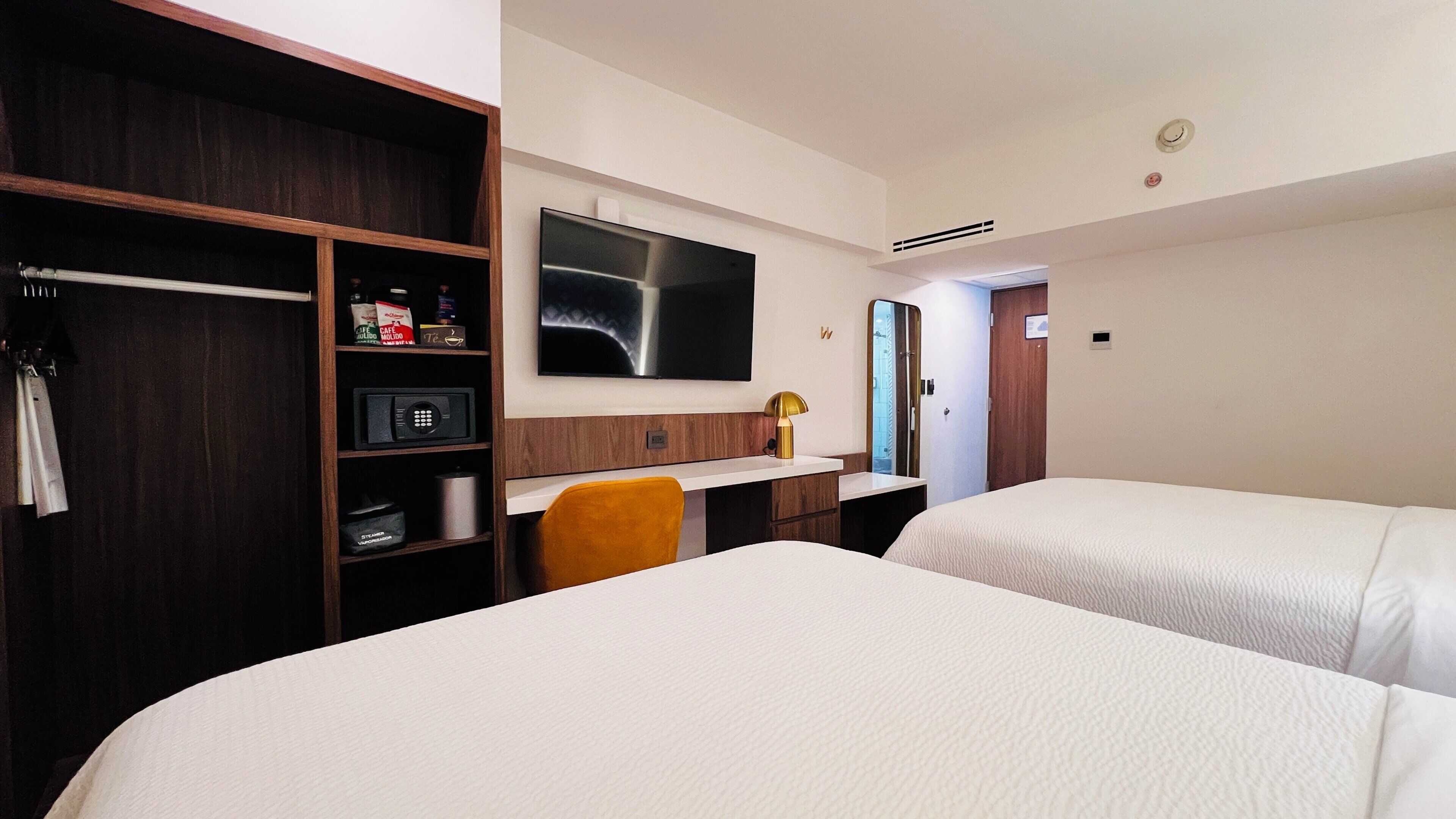 A hotel room with two beds, a desk, a TV, a wardrobe, and a mirror.