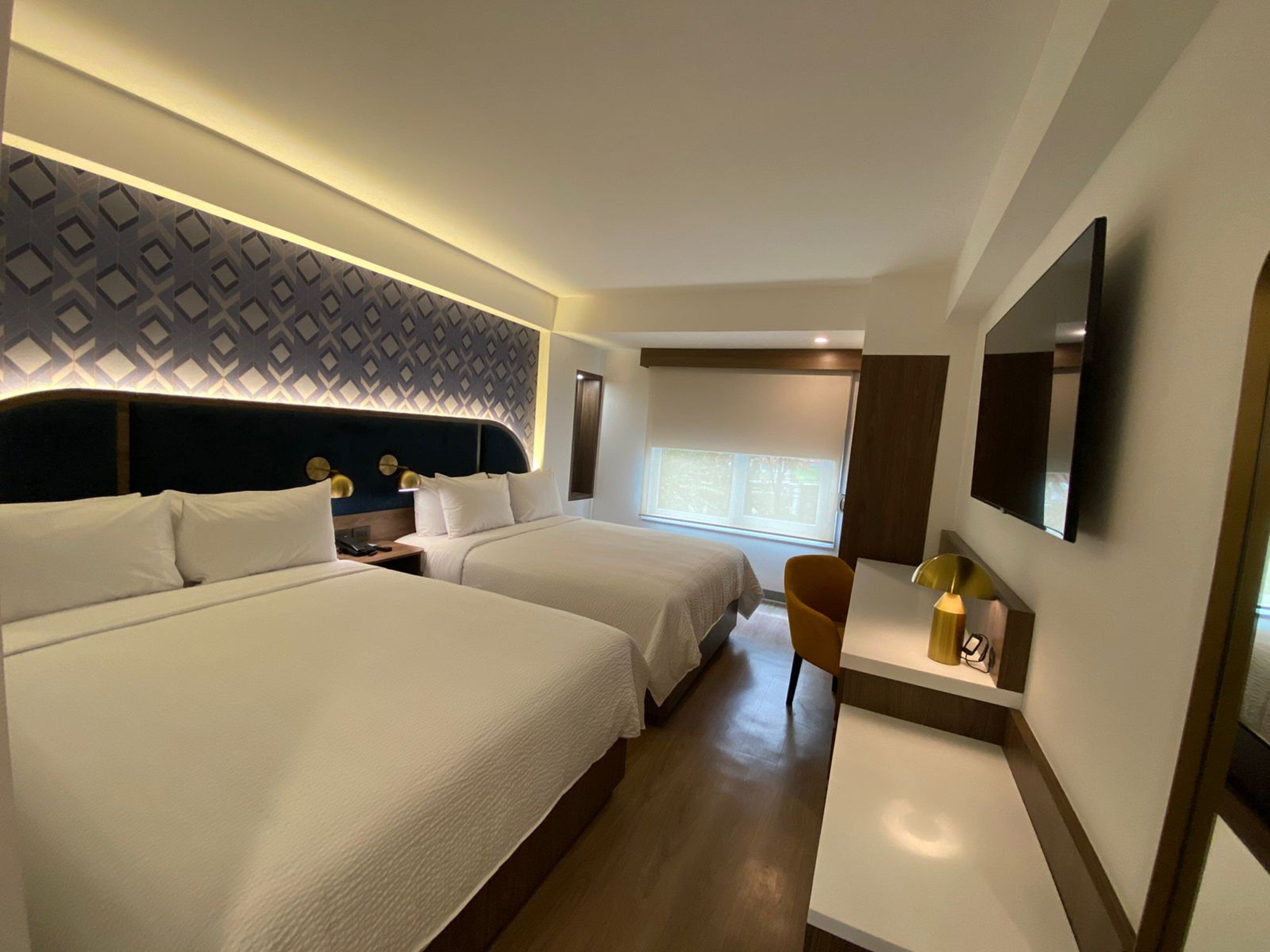 Une chambre d’hôtel avec deux lits, une télévision, un bureau avec une lampe et un mur décoré d’un motif.