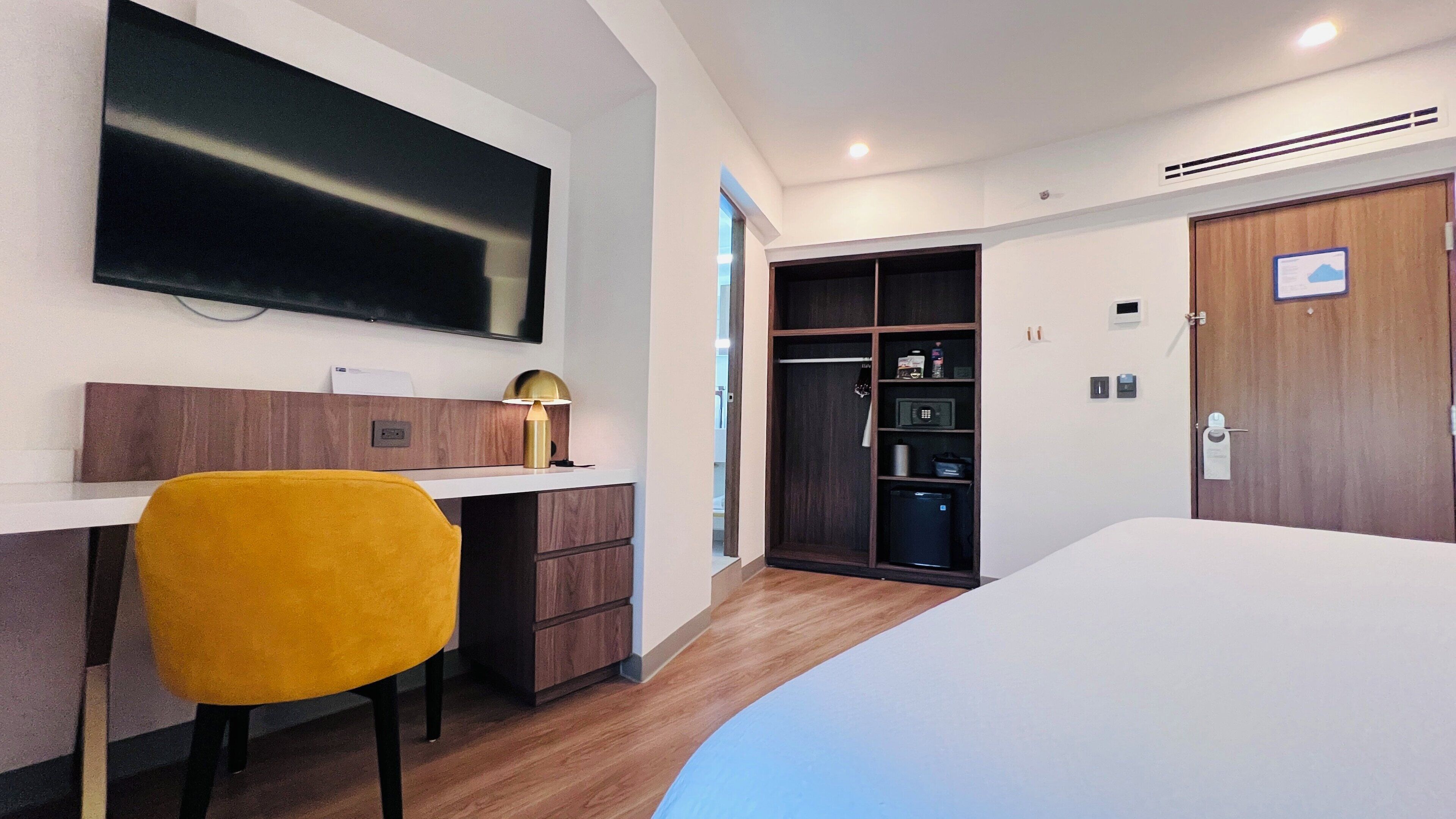 A hotel room with a bed, a desk with a chair, a TV, a wardrobe, and a microwave.