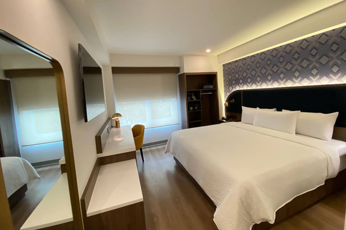 Una habitación de hotel moderna con una cama grande, un escritorio con silla, un armario y un espejo.