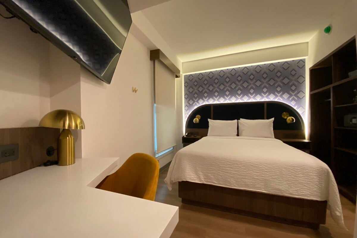 Una habitación de hotel moderna con una cama, un escritorio, una silla y un televisor montado en la pared.