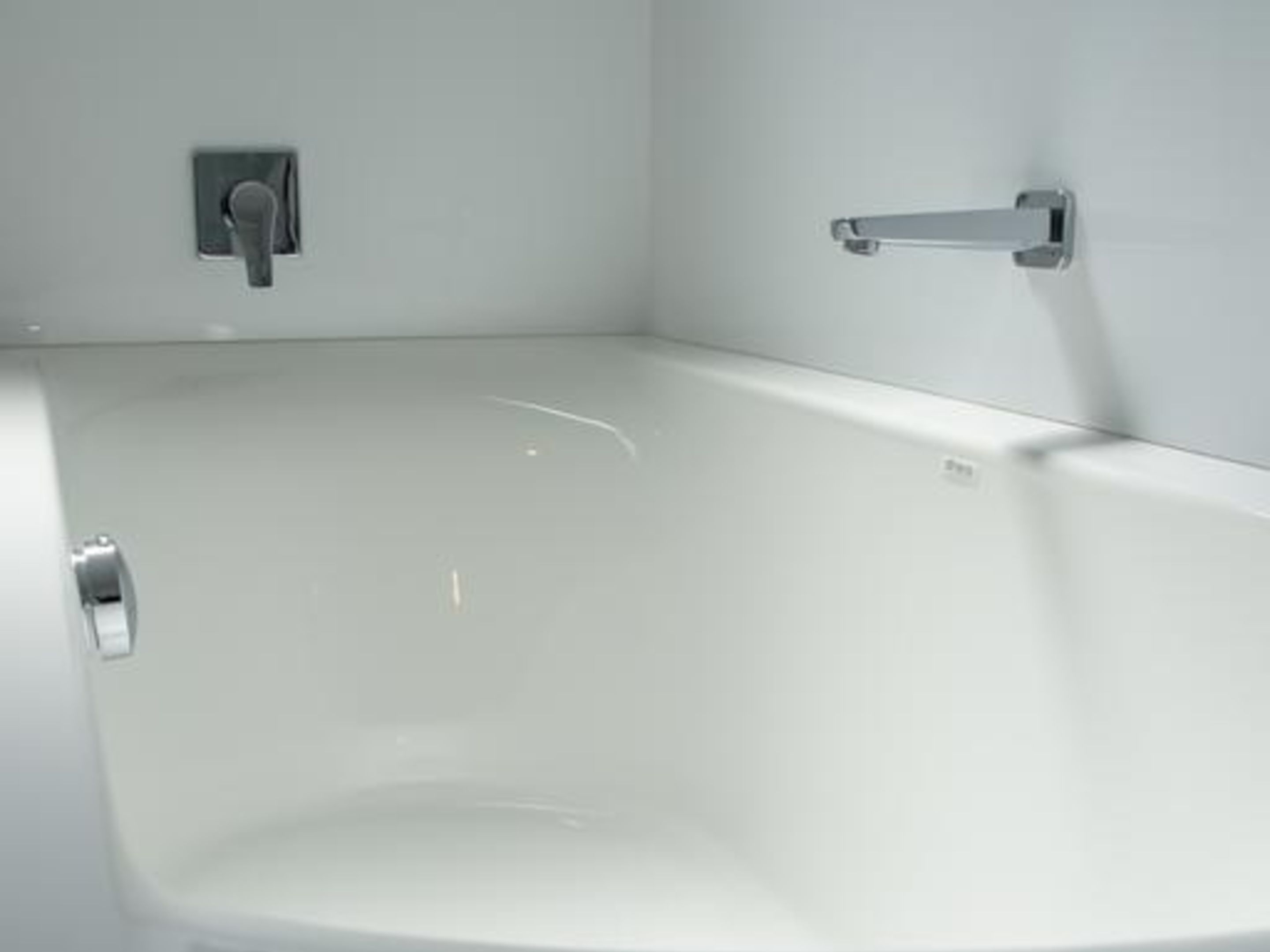 Un baño moderno con una bañera blanca, un cabezal de ducha manual y un grifo empotrado en la pared.