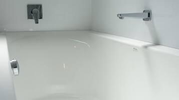 Un baño moderno con una bañera blanca, un cabezal de ducha manual y un grifo empotrado en la pared.