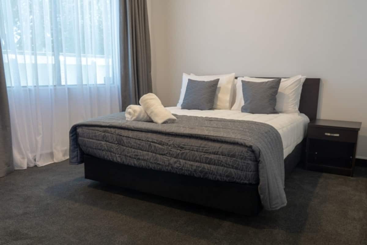 Una cama bien hecha con un cabecero oscuro, un edredón gris y dos almohadas.