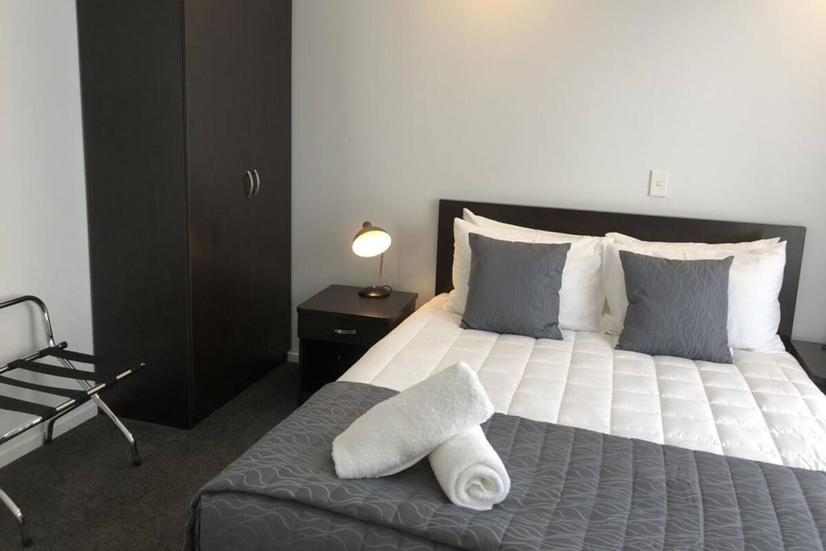 Una habitación de hotel con cama, mesita de noche con lámpara, armario y una silla.