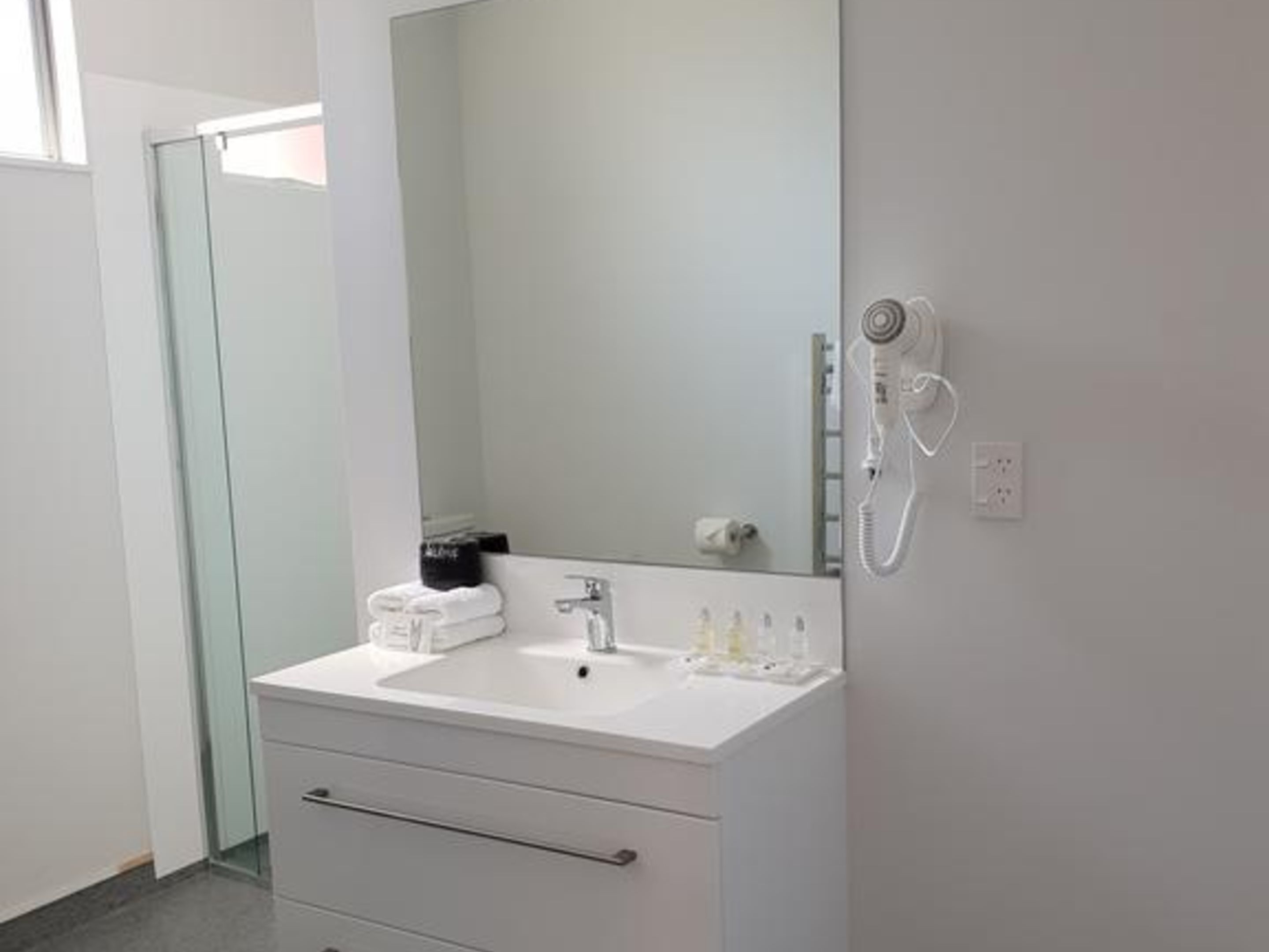 Ein modernes Badezimmer mit einem weißen Waschtisch, einem großen Spiegel und einer integrierten Dusche.