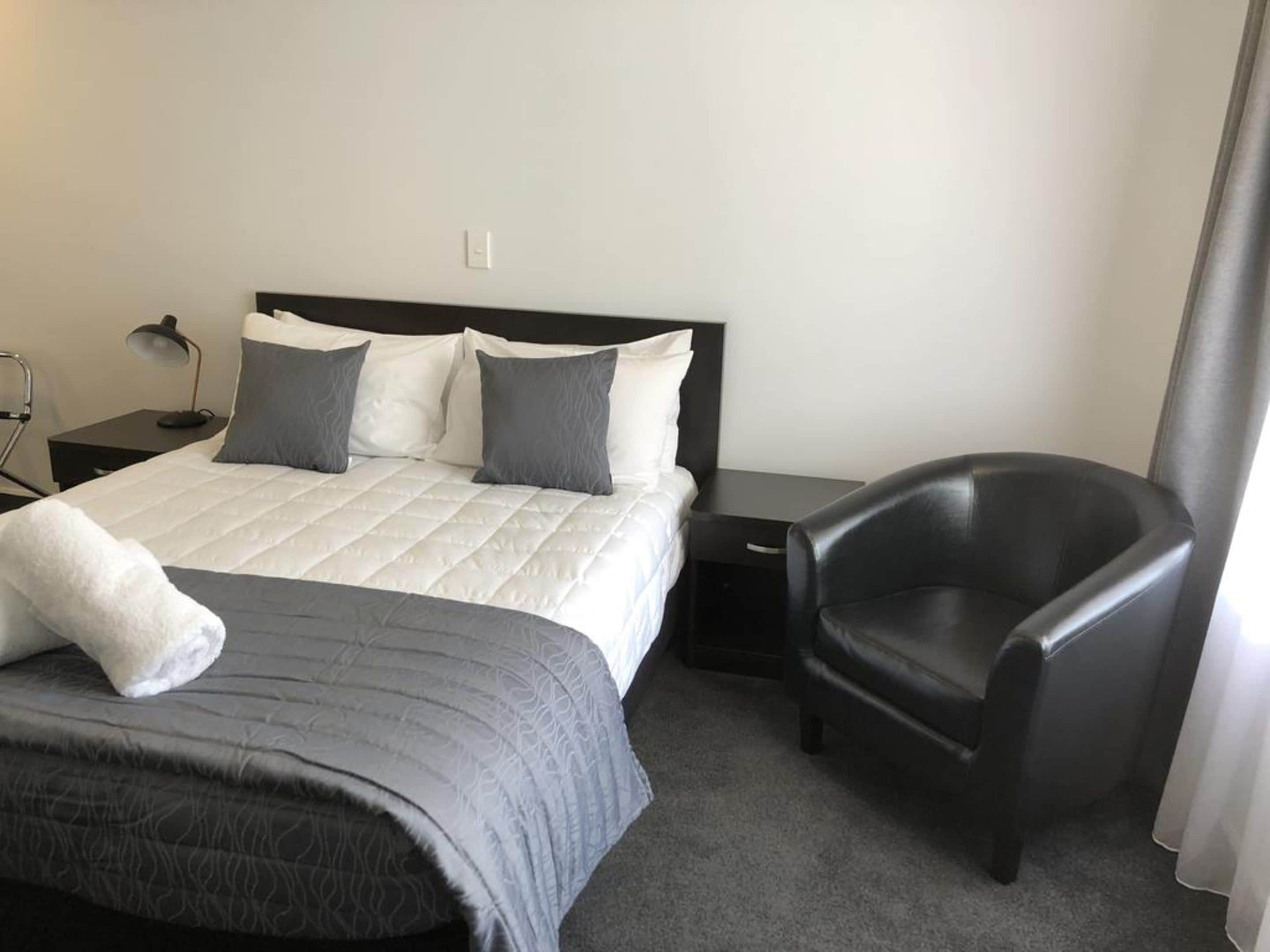 Une chambre d’hôtel avec un lit, une chaise, une table de chevet et une lampe.