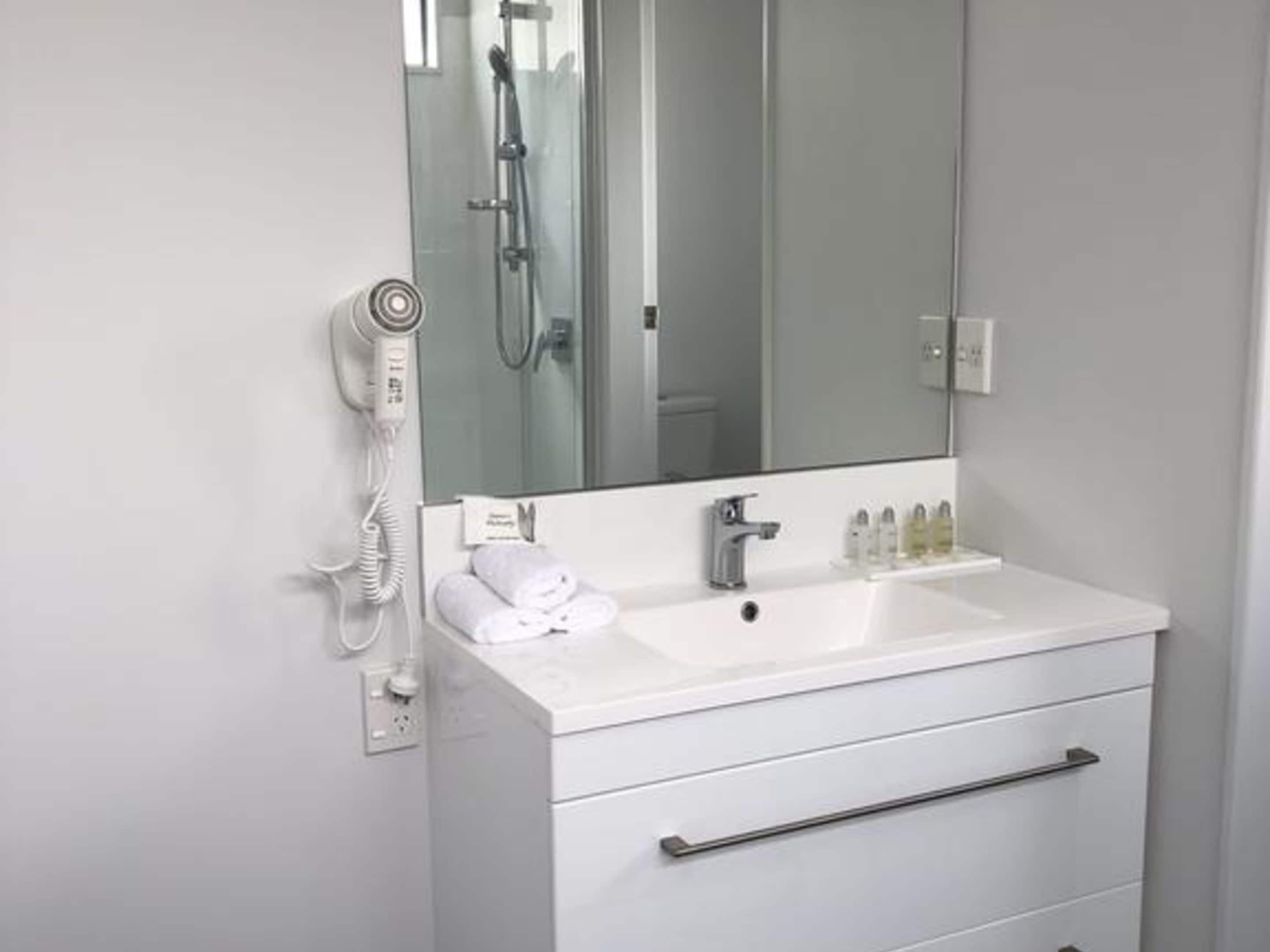 Un baño con lavamanos blanco, espejo, secador de pelo y ducha.