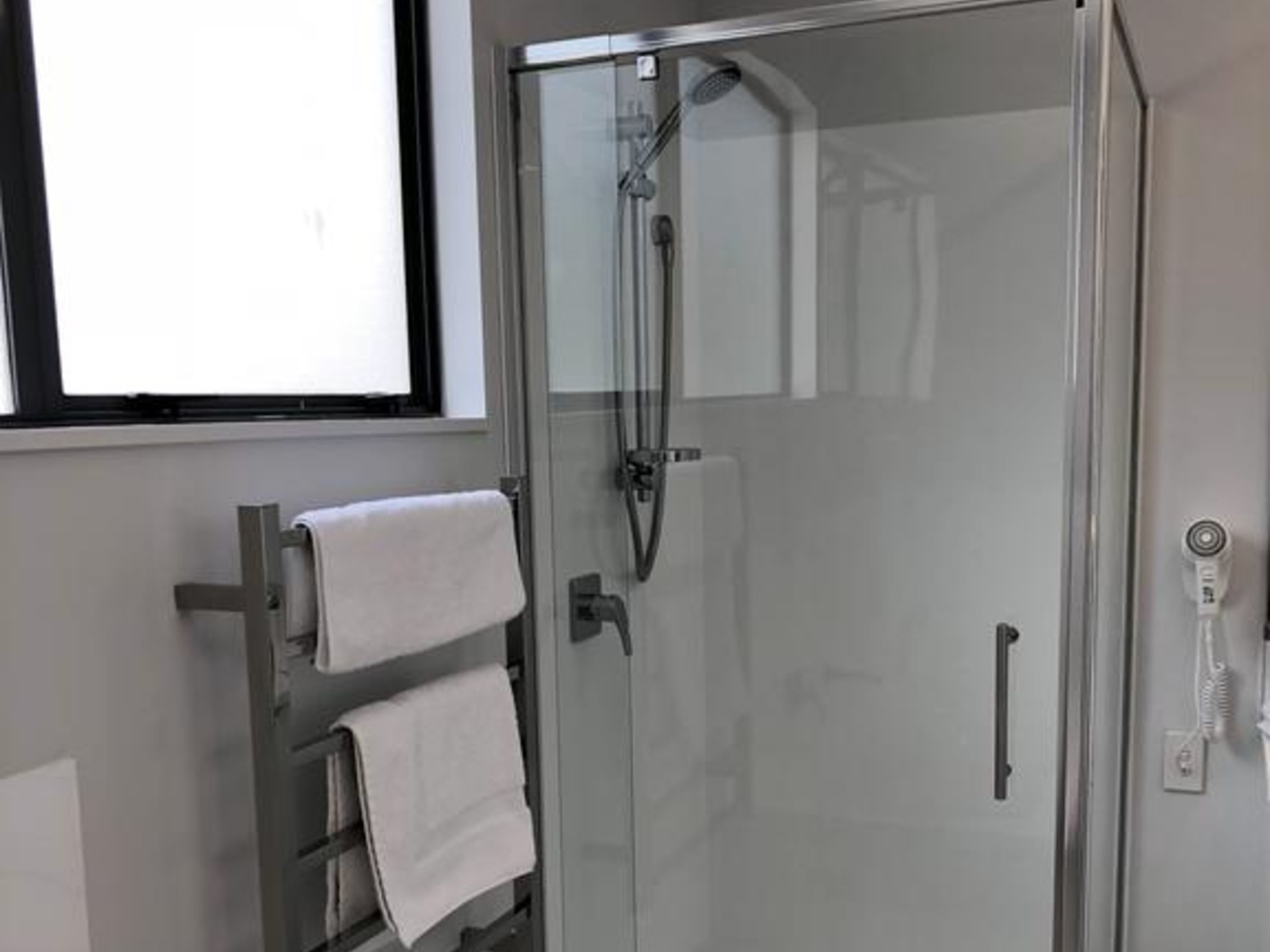 Uma casa de banho moderna com cabine de duche em vidro, um porta-toalhas com duas toalhas e um painel de comandos do duche visível.