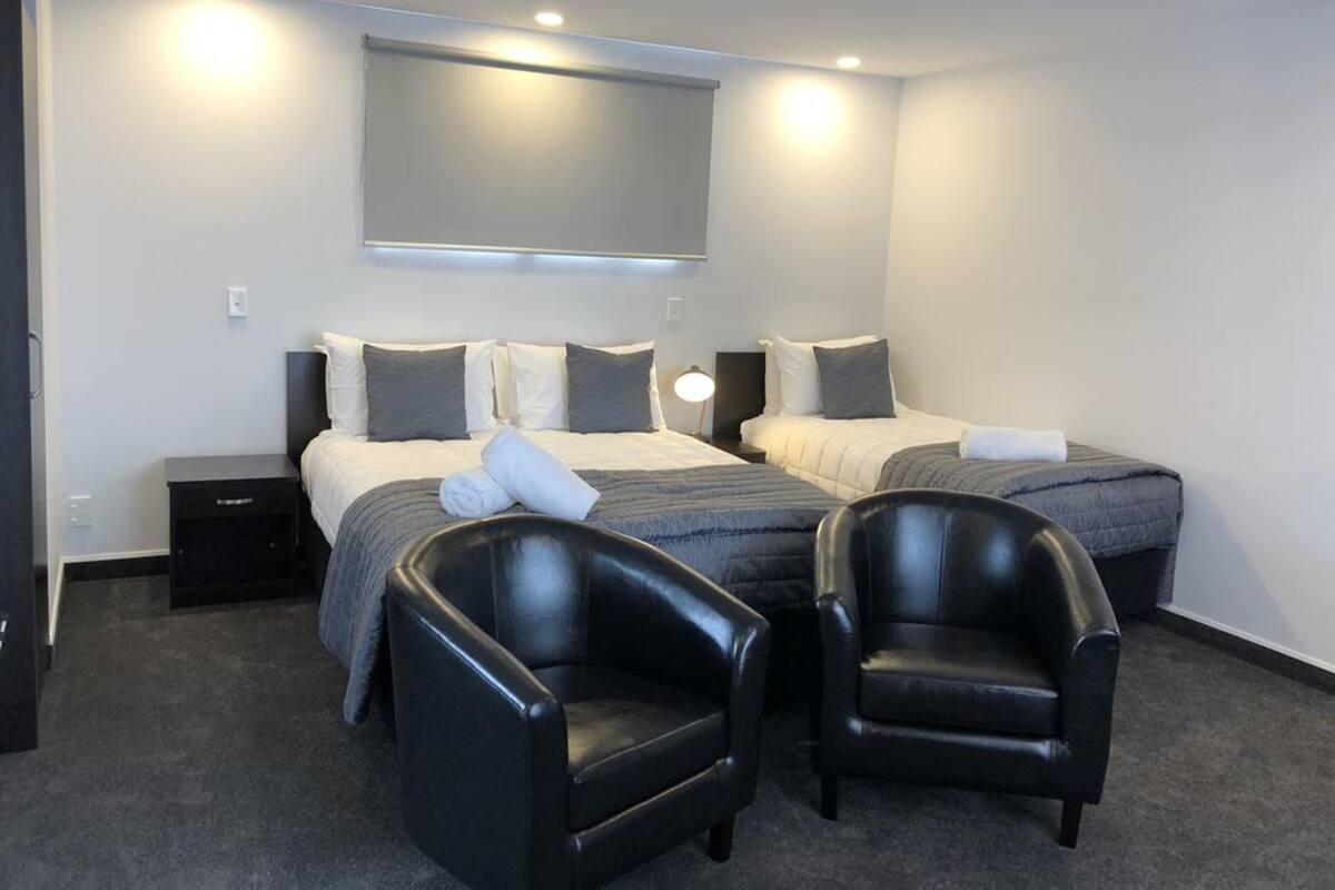 Habitación de hotel con dos camas, un espejo grande, un televisor de pantalla plana y dos sillones de cuero.
