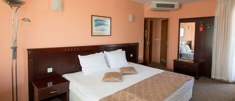Habitación de hotel con una cama grande, una mesita de noche, una lámpara de pie, un cuadro en la pared y un equipo de aire acondicionado.