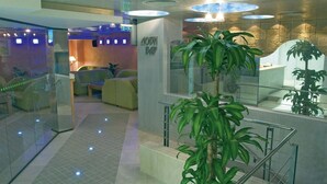 A modern lobby with a reception desk, seating area, and a staircase with glass railings.