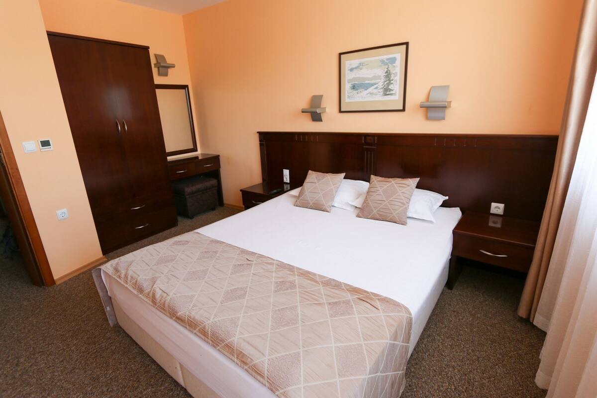 A hotel room with a large bed, a wardrobe, a bedside table, and a framed picture on the wall.