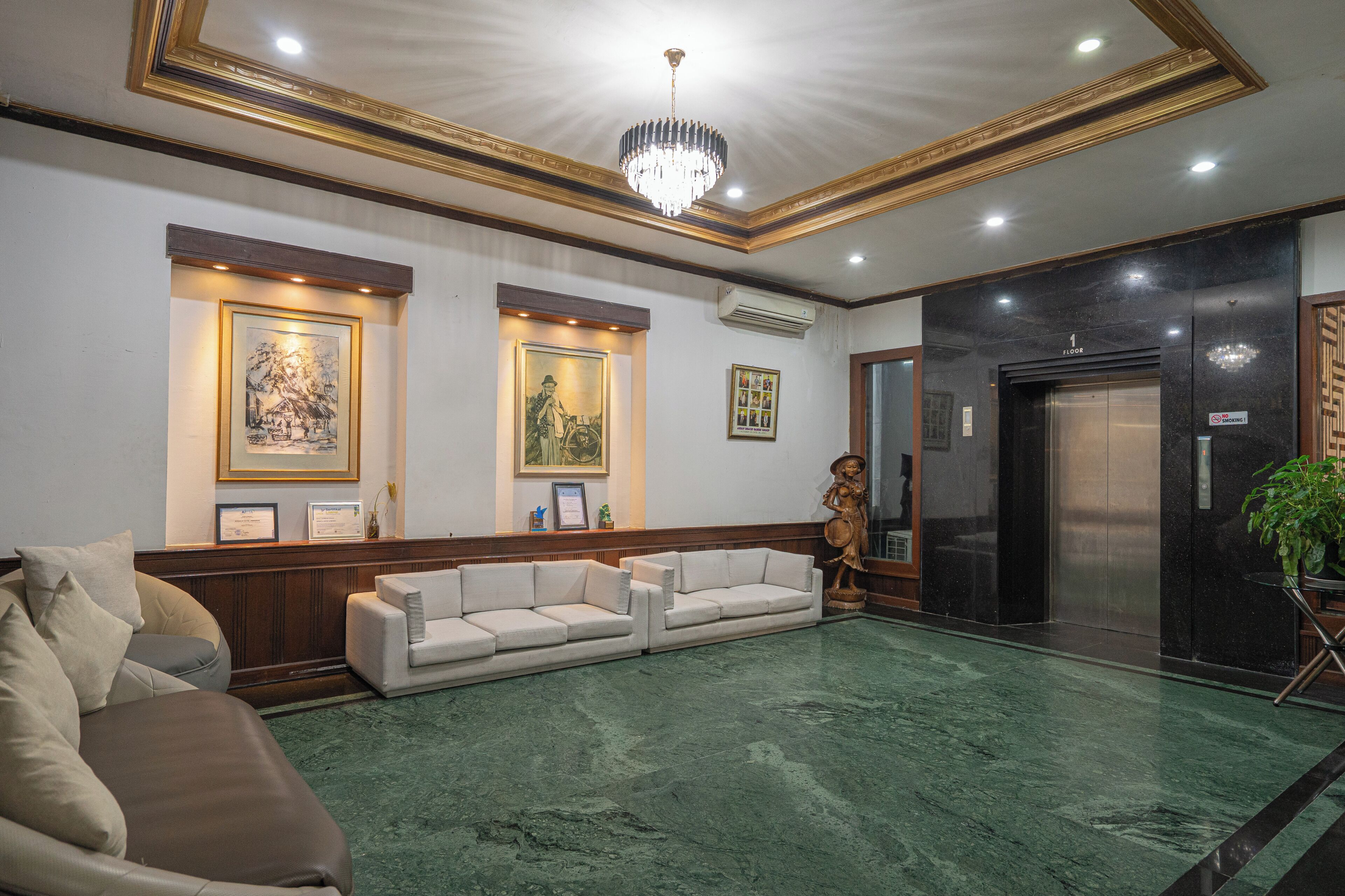 A lobby with a green marble floor, a white sofa, a chandelier, framed artwork, and an elevator.