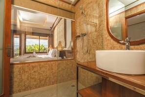 A bathroom with a large mirror, a white sink, and a shower. - Nirmala Heritage Hotel (Jimbaran)