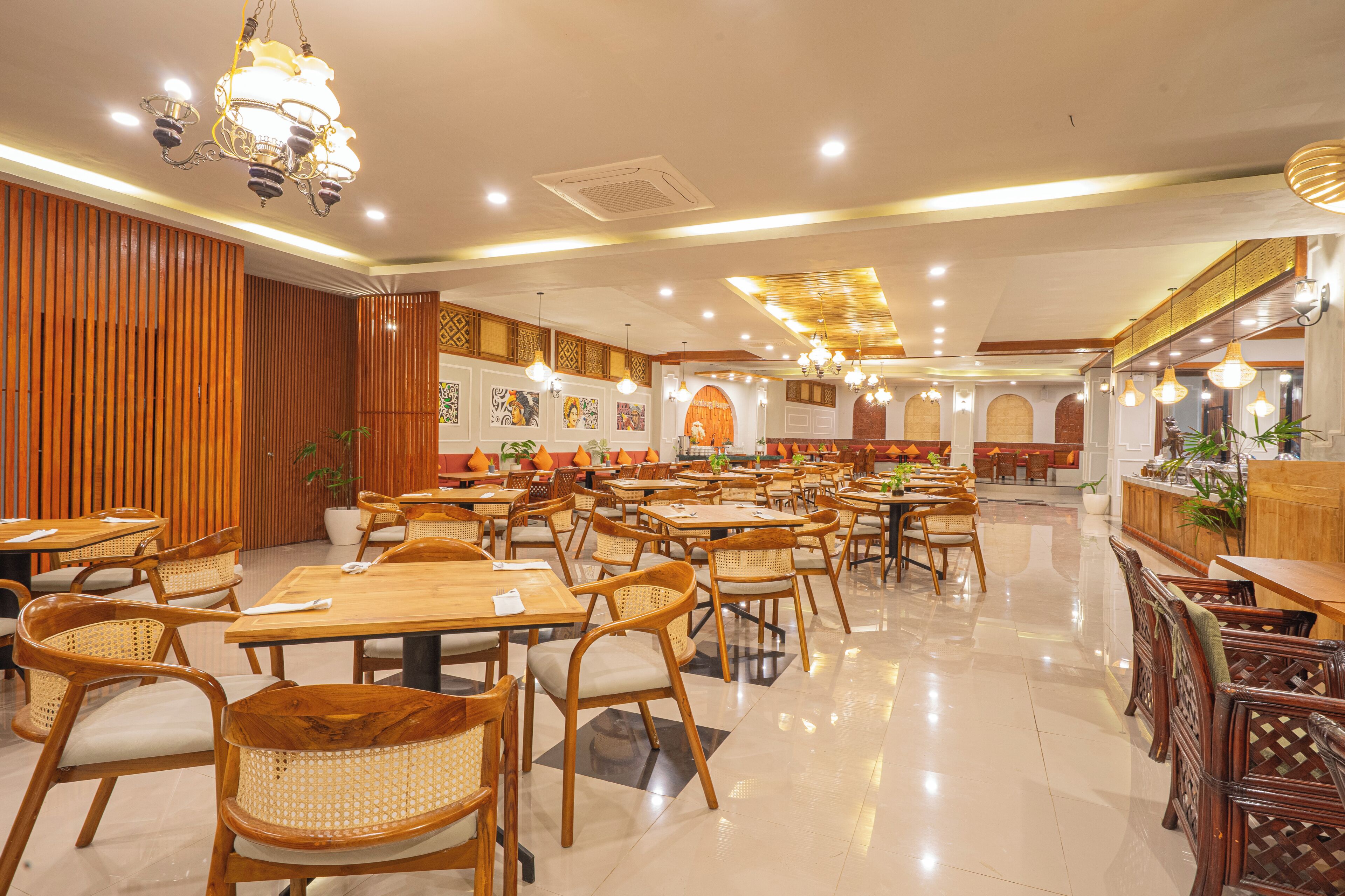 A spacious restaurant with wooden tables and chairs, decorative wall art, and a variety of hanging lights.