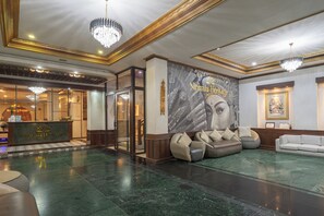 A hotel lobby with a reception desk, seating areas, chandeliers, and a mural. - Nirmala Heritage Hotel (Jimbaran)