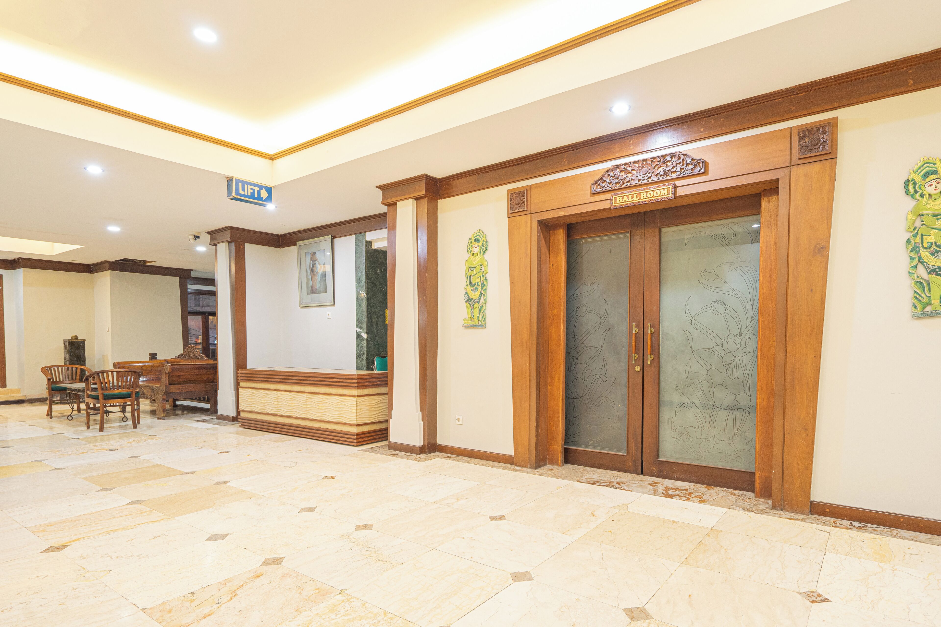 A hotel lobby with a reception desk, a lift sign, a bar room sign, and a decorative wall piece.