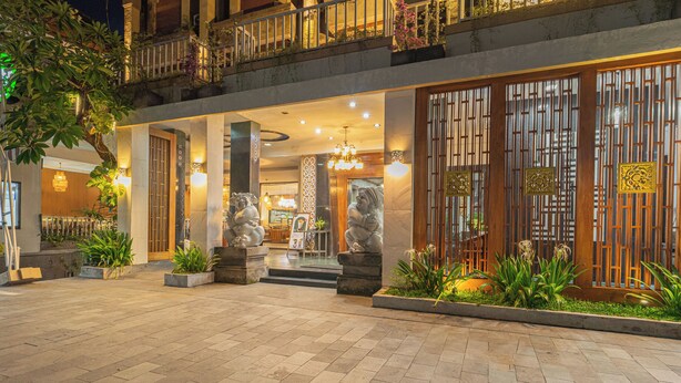 A hotel entrance with a tiled courtyard, stone statues, and a traditional wooden gate. - Nirmala Heritage Hotel (Jimbaran)