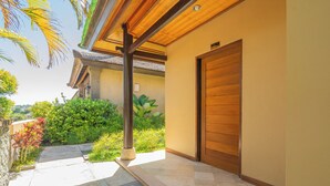 A covered outdoor area with a wooden door, a stone pillar, and a tiled floor. - Nirmala Heritage Hotel (Jimbaran)