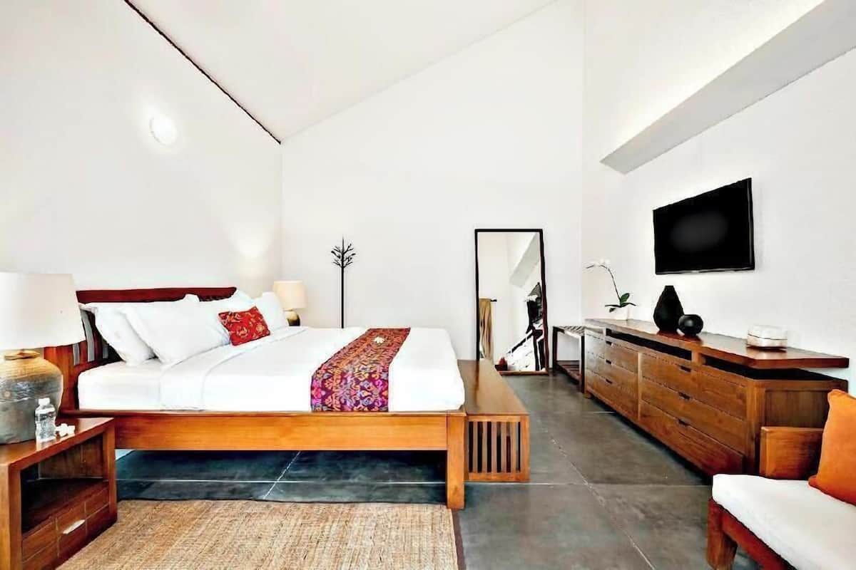 Ein modernes Schlafzimmer mit einem Bett, Nachttischen, einer Kommode, einem Fernseher und einem Spiegel.