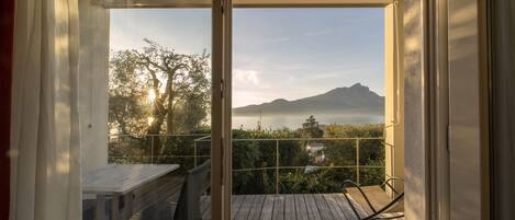 A wooden deck with a table and chairs, a glass door leading to a balcony with a view of a mountain and trees.
