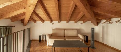 A spacious loft with a high wooden ceiling, a sofa, a coffee table, and a standing heater.