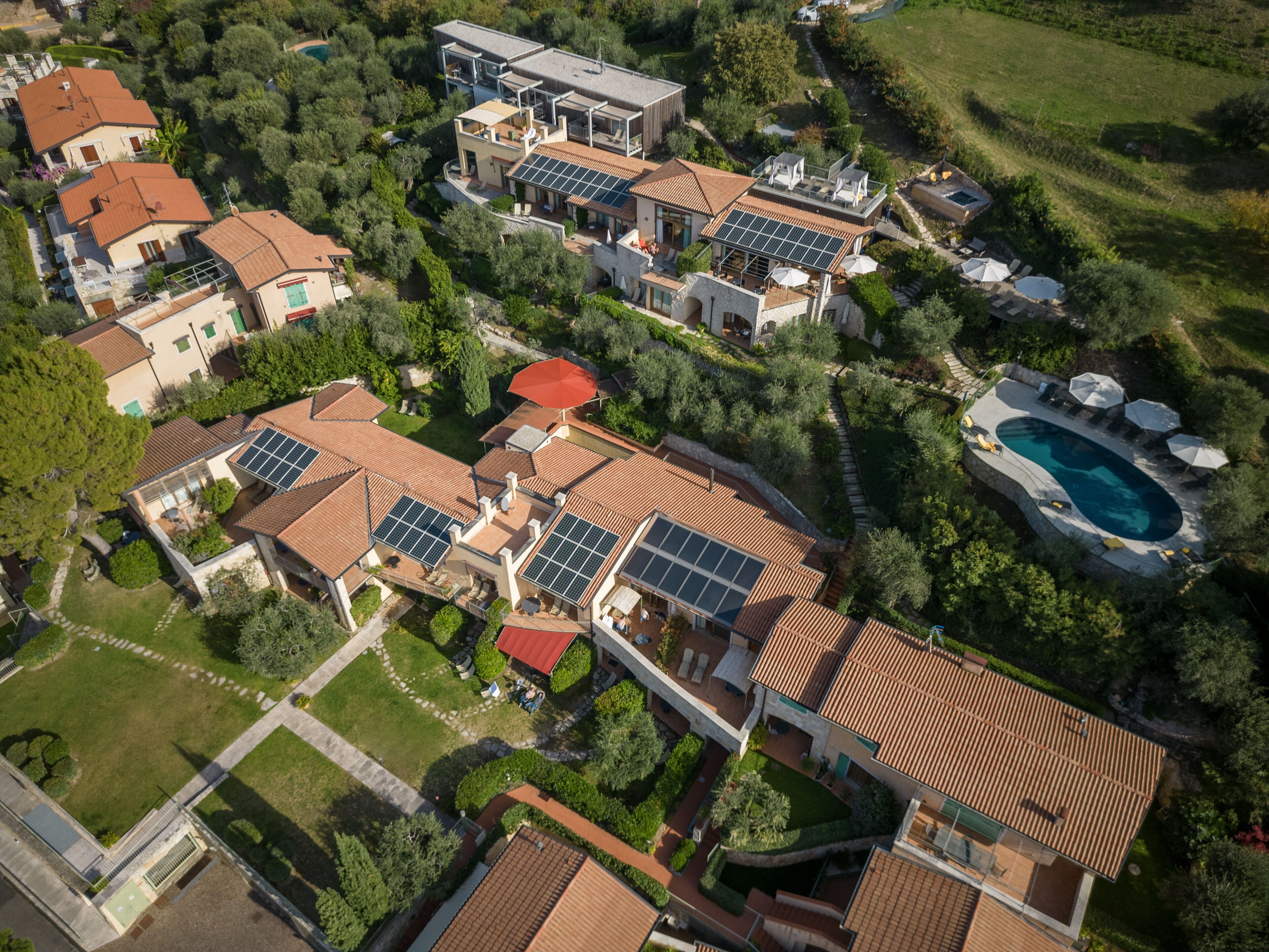 An aerial view of a residential area with multiple houses, solar panels, a swimming pool, and well-maintained gardens.