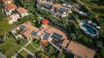 An aerial view of a residential area with multiple houses, solar panels, a swimming pool, and well-maintained gardens.