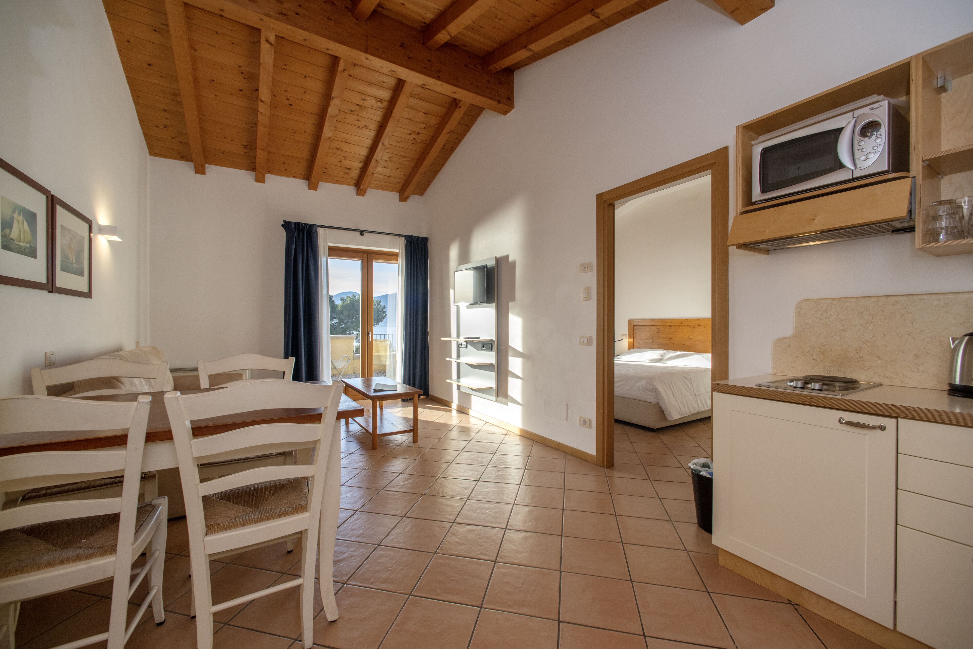 Een ruime kamer met houten plafond, een eethoek met witte stoelen, een keuken met een magnetron en een bed met uitzicht.