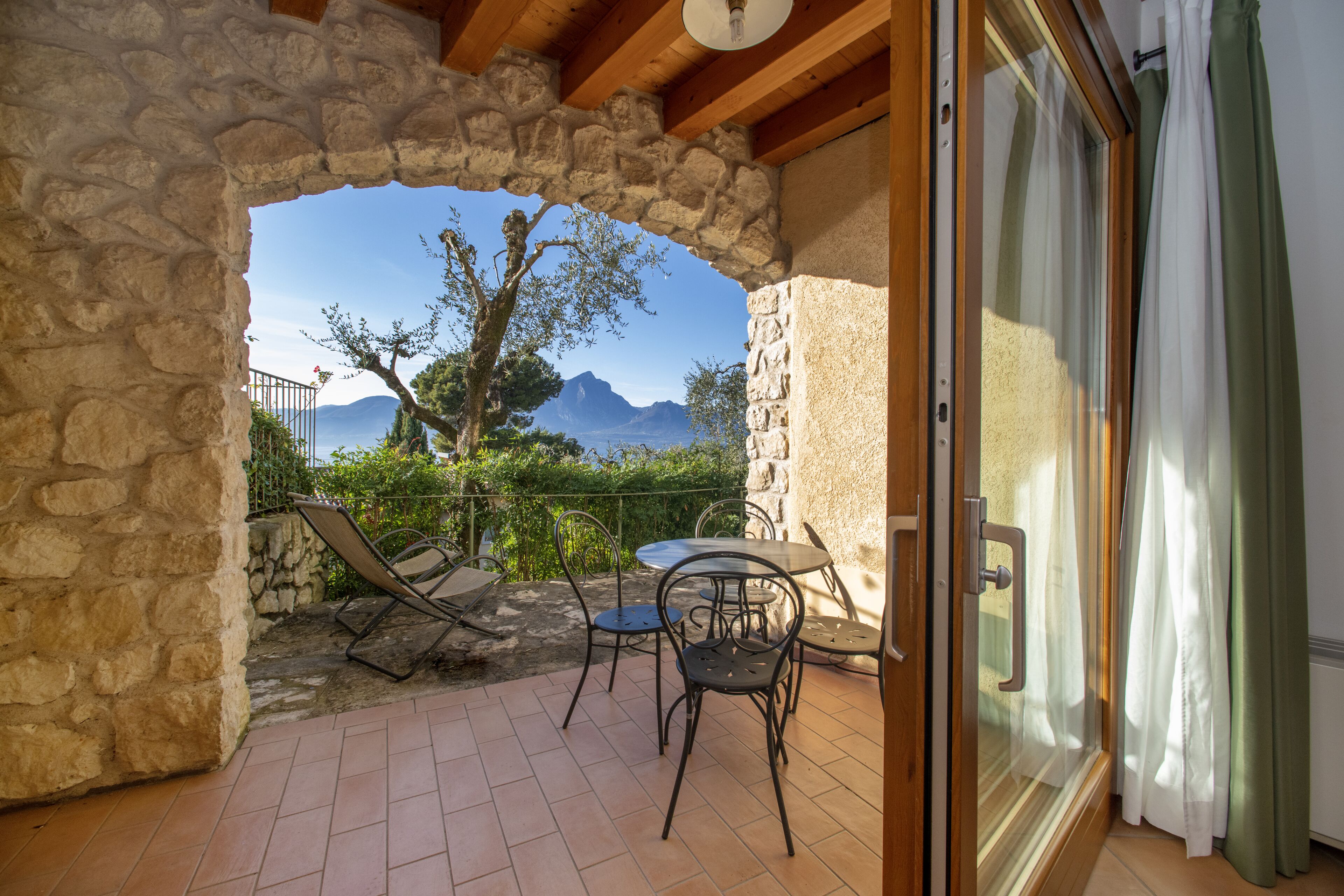 A stone-framed balcony with a table and chairs, overlooking a mountainous landscape.