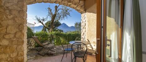 A stone-framed balcony with a table and chairs, overlooking a mountainous landscape.