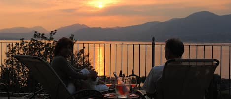 Two people seated at a table with a view of a sunset over a body of water and mountains.